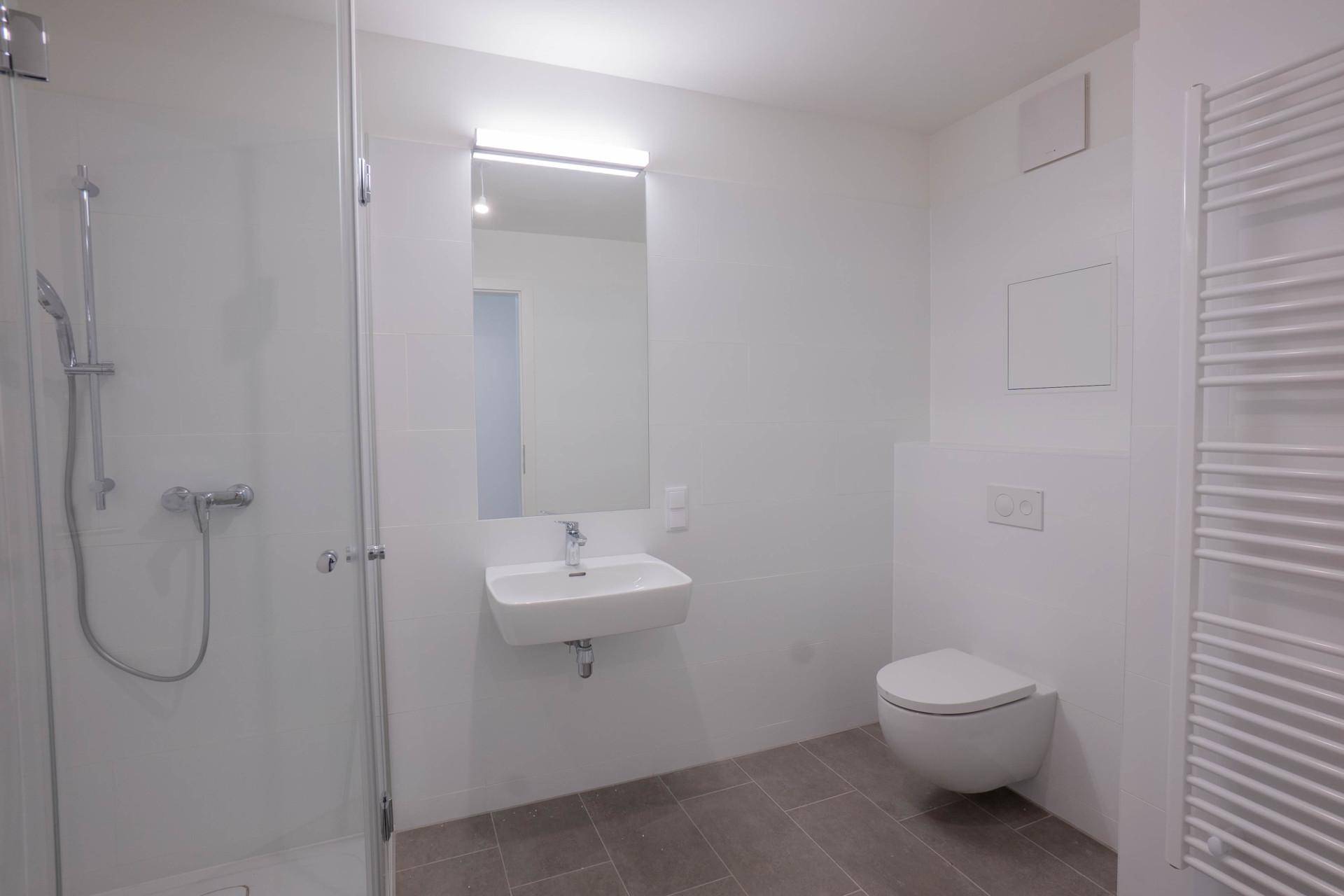Modernes Badezimmer mit ebenerdiger Dusche, Wand-WC und beheiztem Handtuchhalter.
