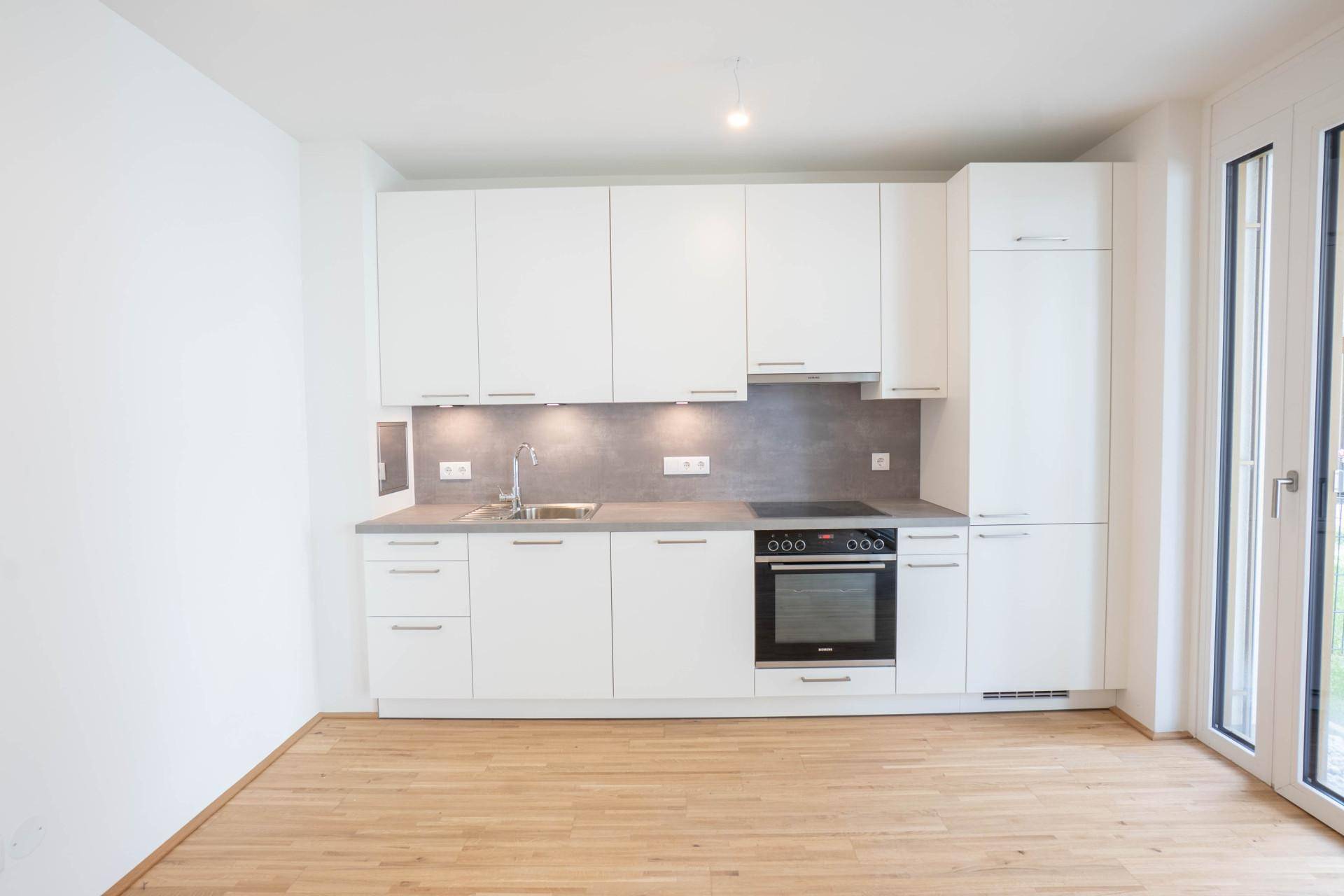 Helle, moderne Einbauküche in Weiß mit Holzfußboden und Zugang zur Terrasse.