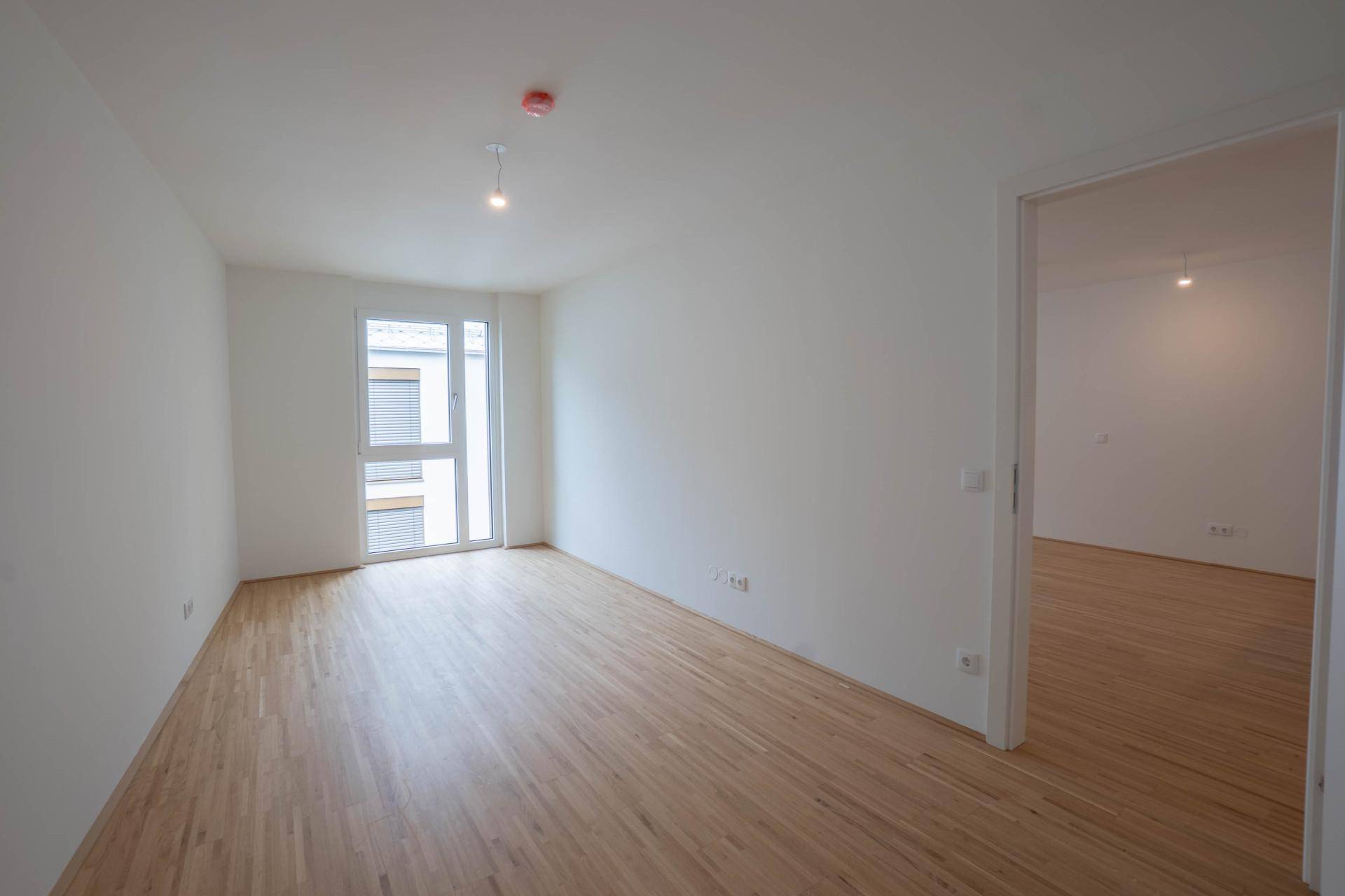 Helles Schlafzimmer mit Parkettboden und großem Fenster.