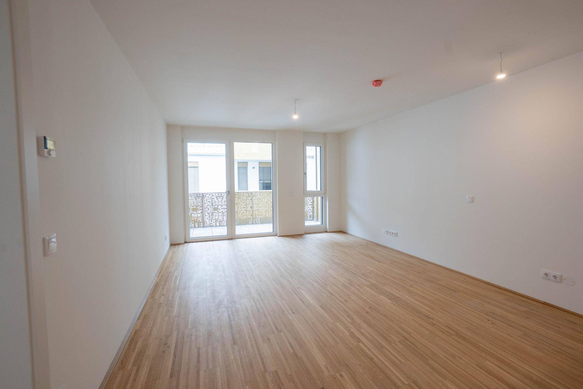 Geräumiger, heller Wohnraum mit Parkettboden und Zugang zum Balkon.