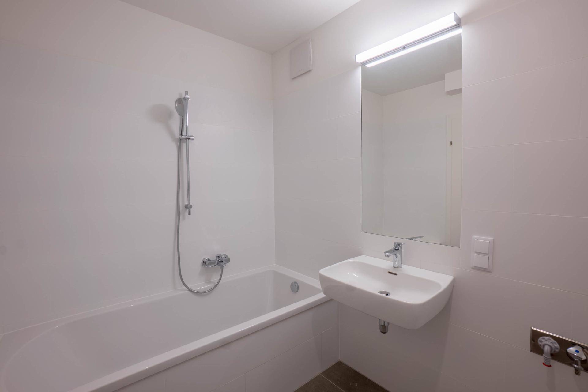 Modernes Badezimmer mit Badewanne, Einzelwaschbecken und großem Spiegel in hellen Fliesen.