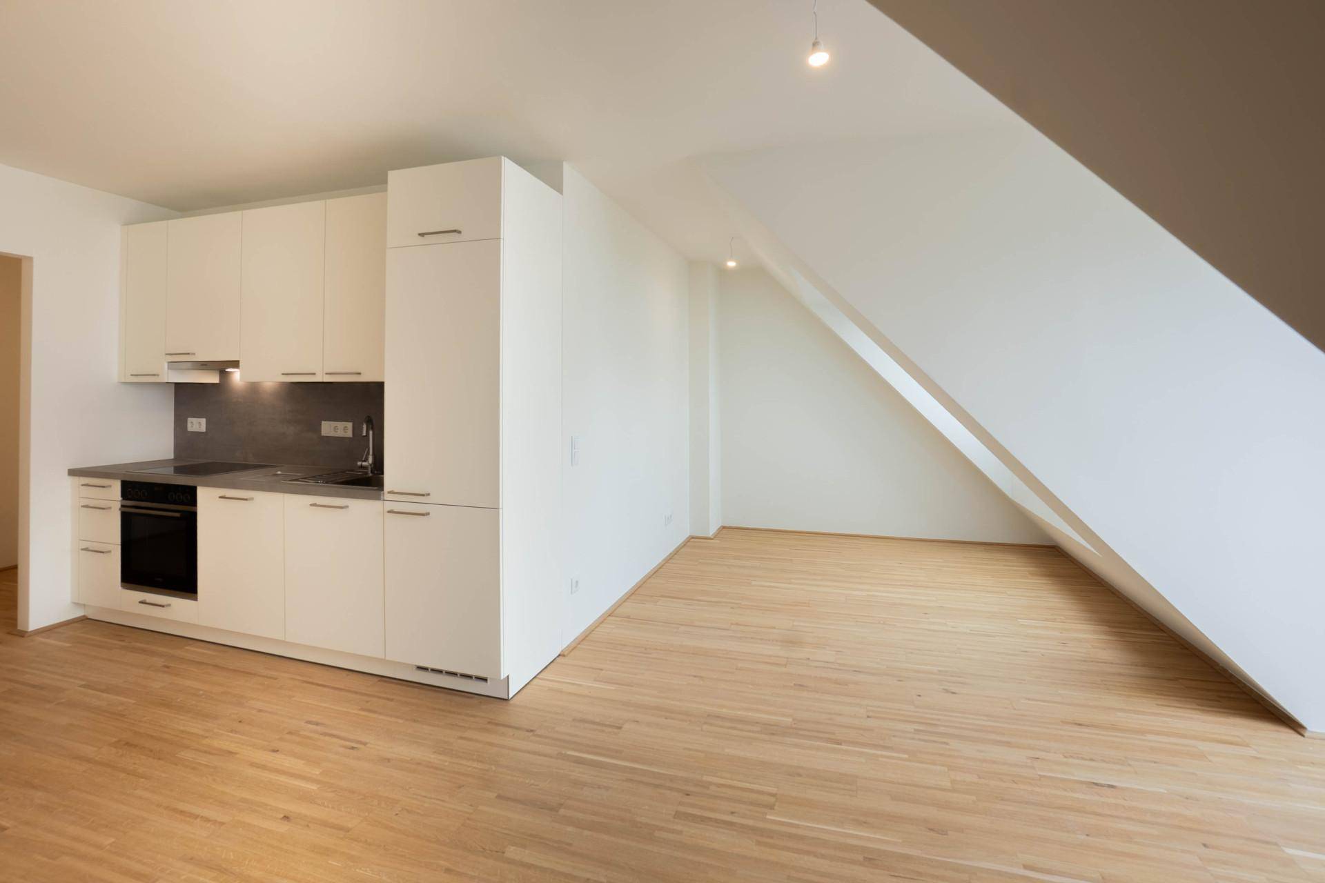 Moderne Küche mit weißen Fronten und integrierten Geräten in einem hellen Raum mit Dachschräge und Holzboden.