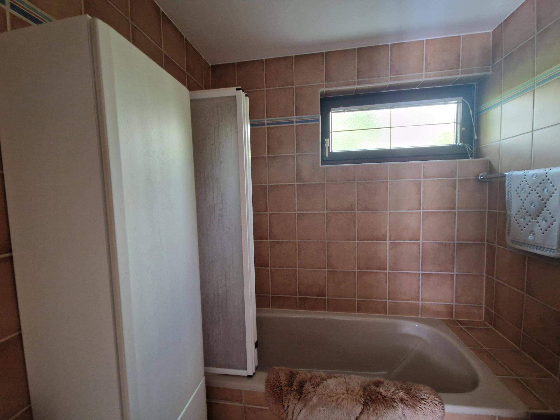 Badezimmer mit braunen Fliesen, Badewanne und kleinem Fenster.