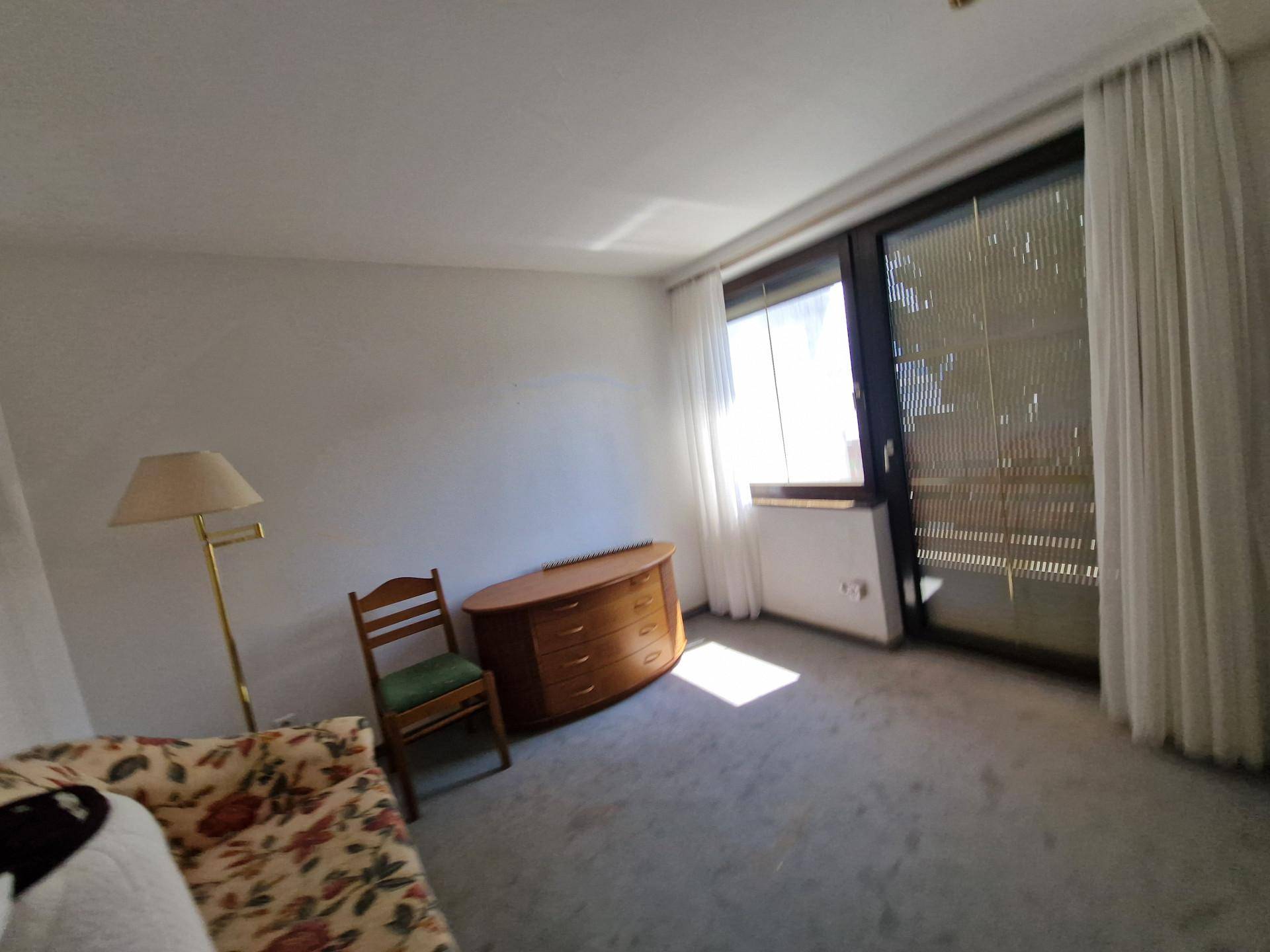 Heller Raum mit Teppichboden und großem Fenster, das viel Tageslicht hereinlässt.