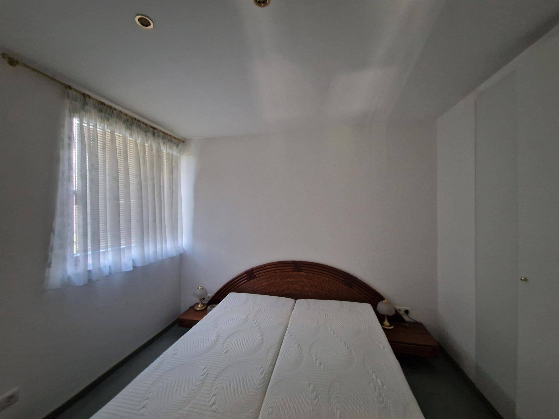 Schlafzimmer mit Doppelbett, Nachttischen und Fenster mit Vorhängen.