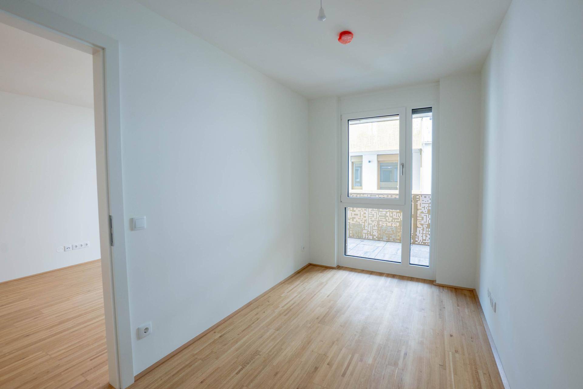 Helles Zimmer mit Holzboden und großem Fenster, das viel Tageslicht hereinlässt.