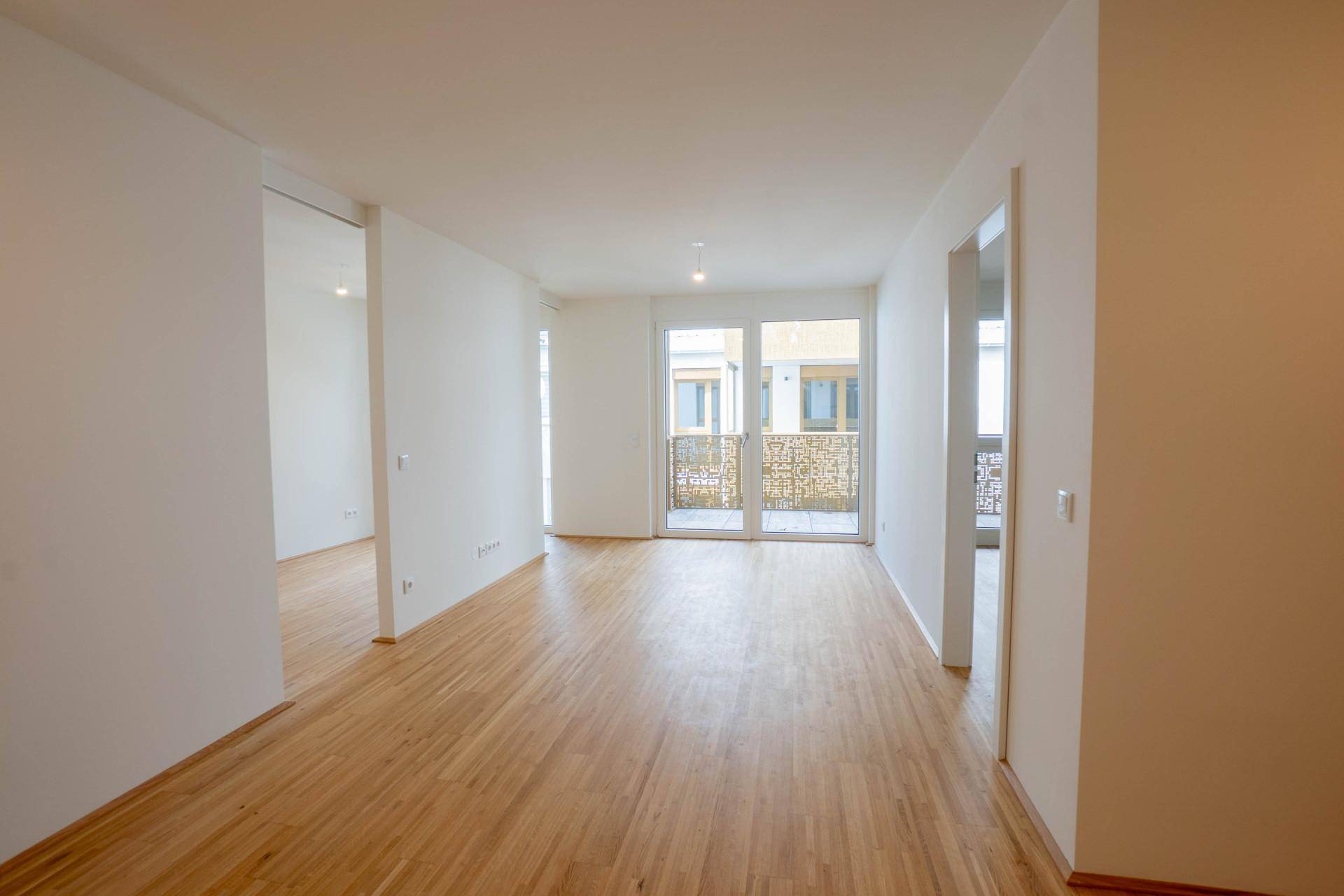 Heller, leerer Wohnbereich mit Holzboden und Zugang zu einem französischen Balkon.
