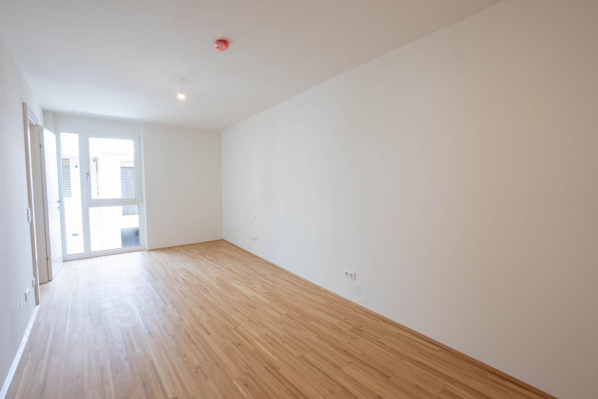 Helles Schlafzimmer mit Parkettboden und Zugang zu einem kleinen Balkon oder einer Terrasse.