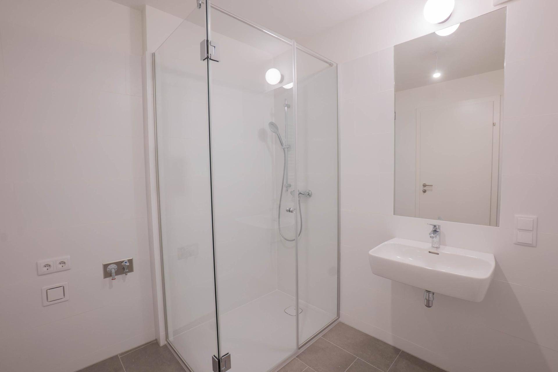 Modernes Badezimmer mit Glasdusche, wandhängendem Waschbecken und großem Spiegel.