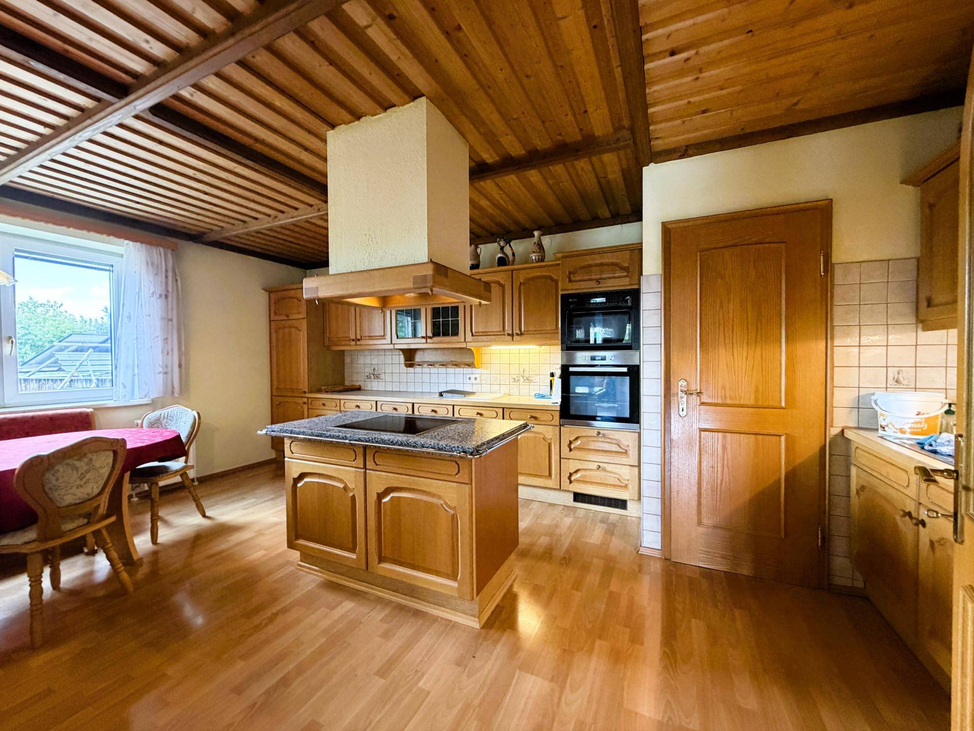 Geräumige Holzküche mit Essbereich, Kücheninsel und integrierten Geräten unter einer Holzdecke.