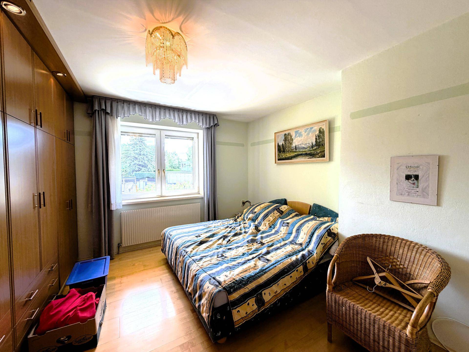 Schlafzimmer mit Holzboden, Einbauschränken und einem großen Fenster mit Blick ins Grüne.