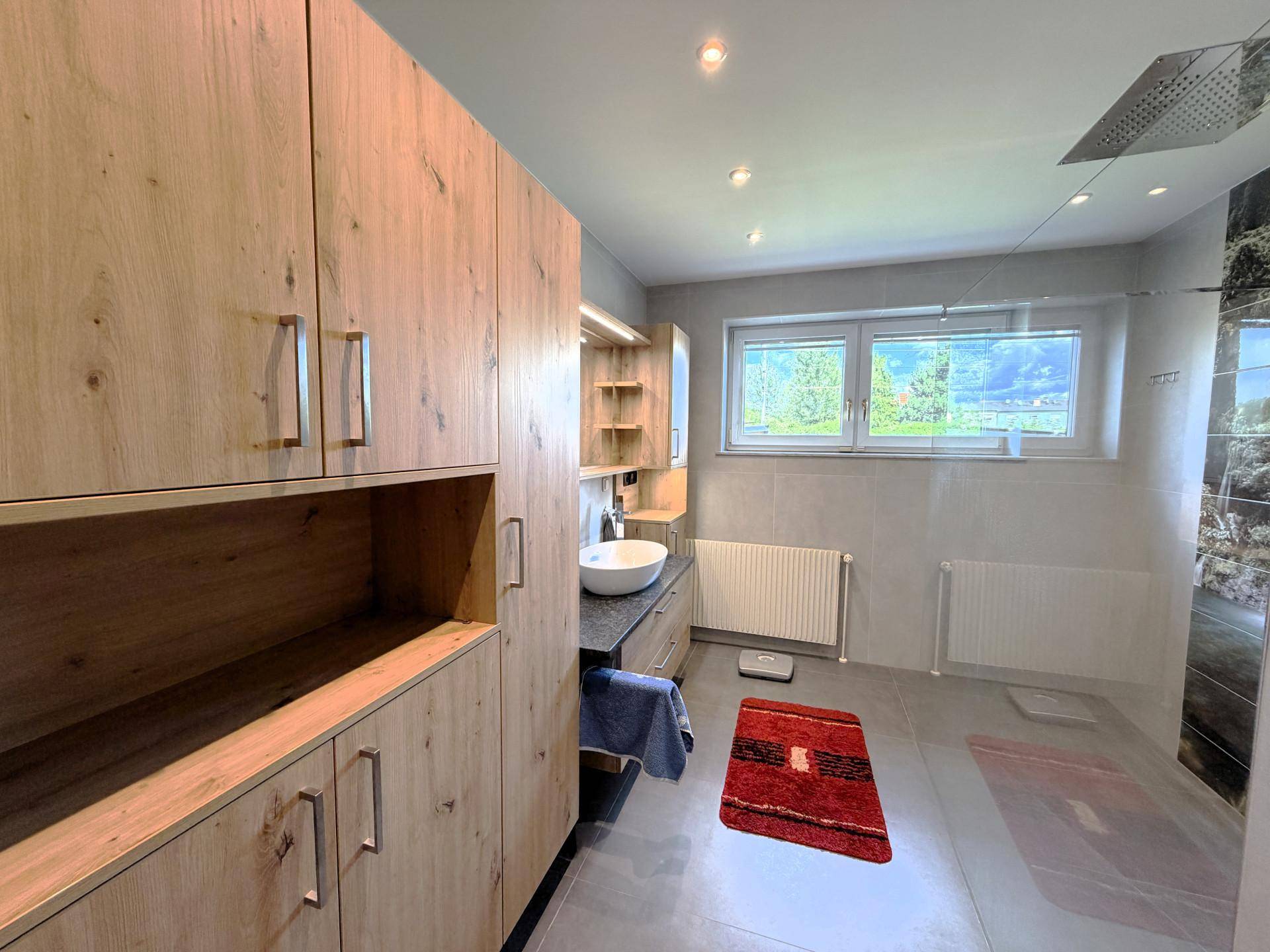 Modernes Badezimmer mit begehbarer Dusche, Holzschränken und großem Fenster.