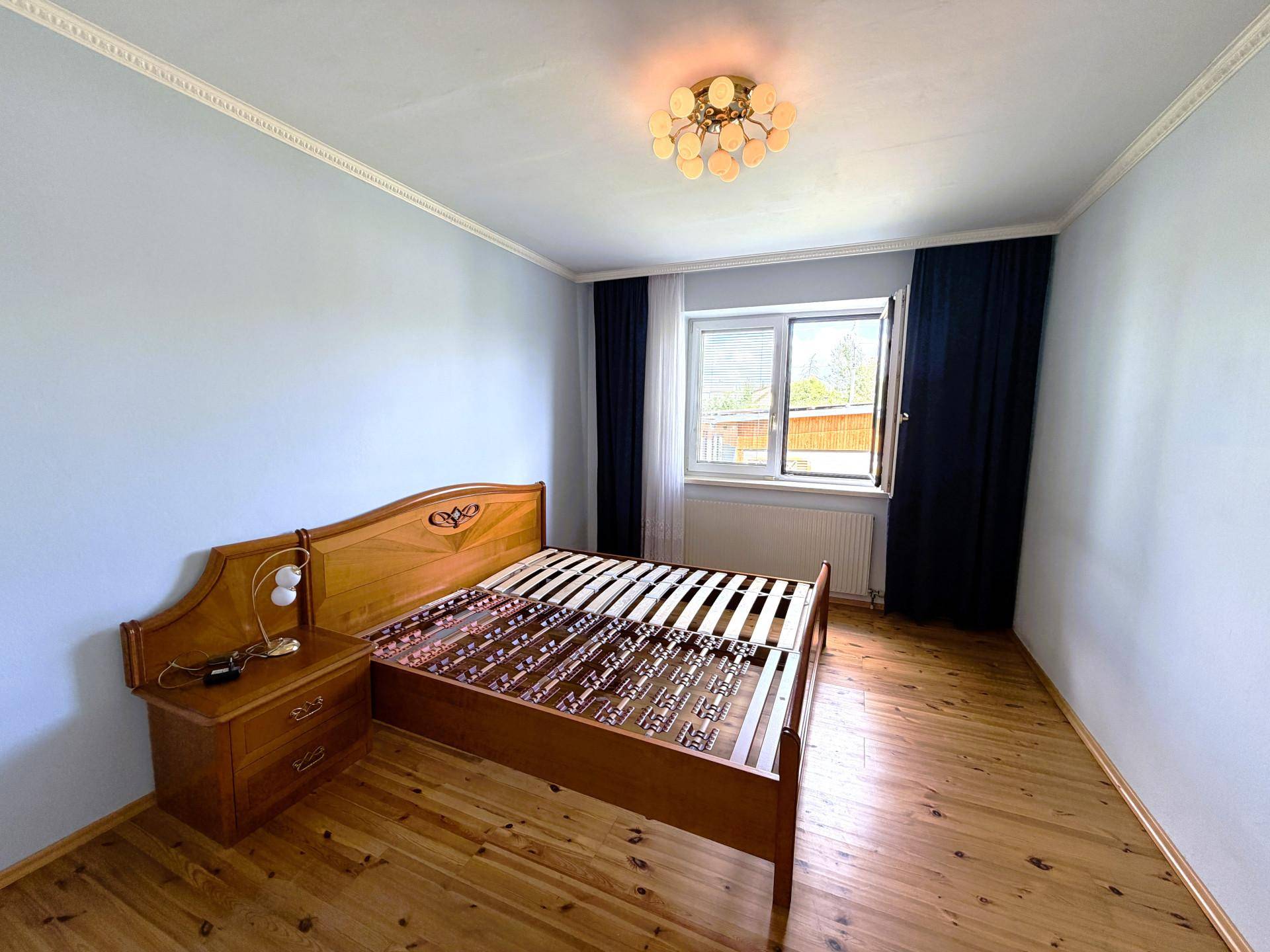 Helles Schlafzimmer mit Holzboden, schlichtem Bettrahmen und einem Fenster mit Blick nach draußen.
