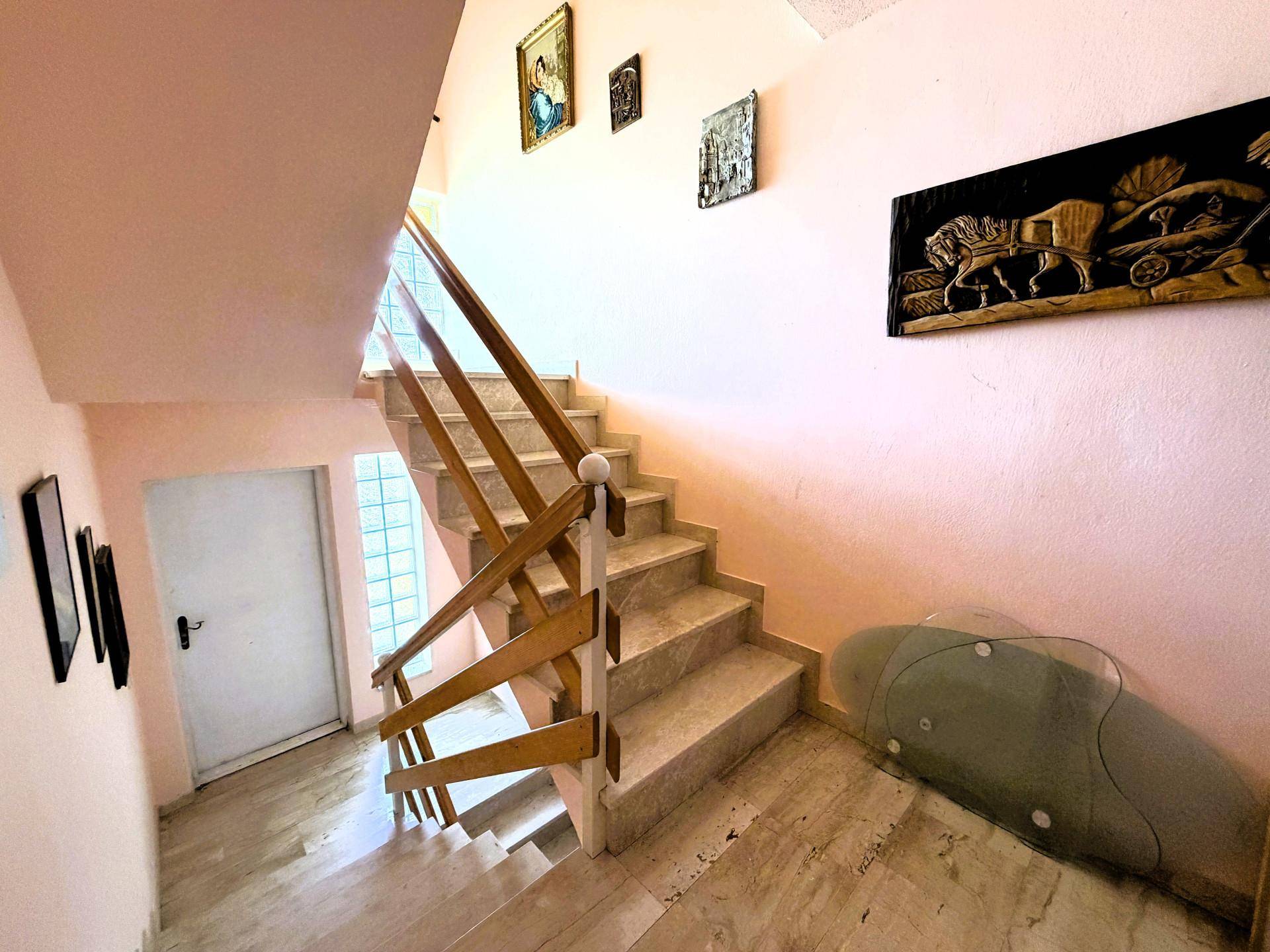 Treppenhaus mit Marmorstufen, Holzgeländer und rosa gestrichenen Wänden.