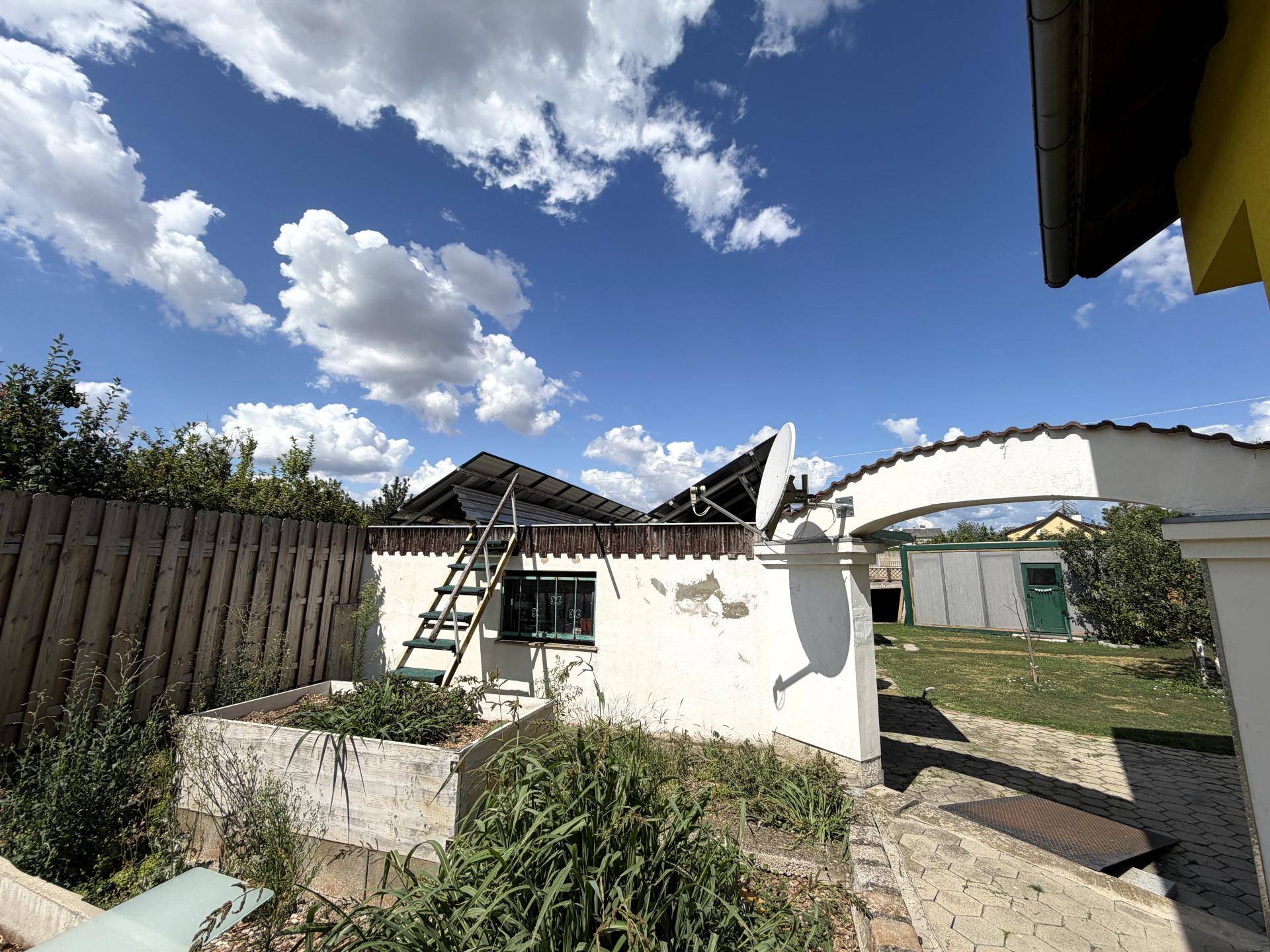 Gartenbereich mit Hochbeeten, Zaun und einem Nebengebäude mit Solaranlage.