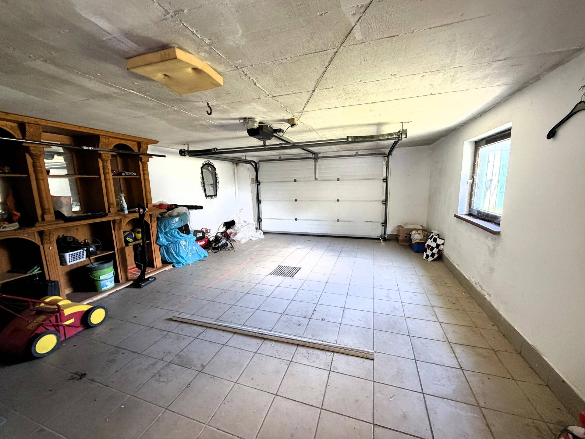 Geräumige Garage mit Fliesenboden, Rolltor und einem Fenster.