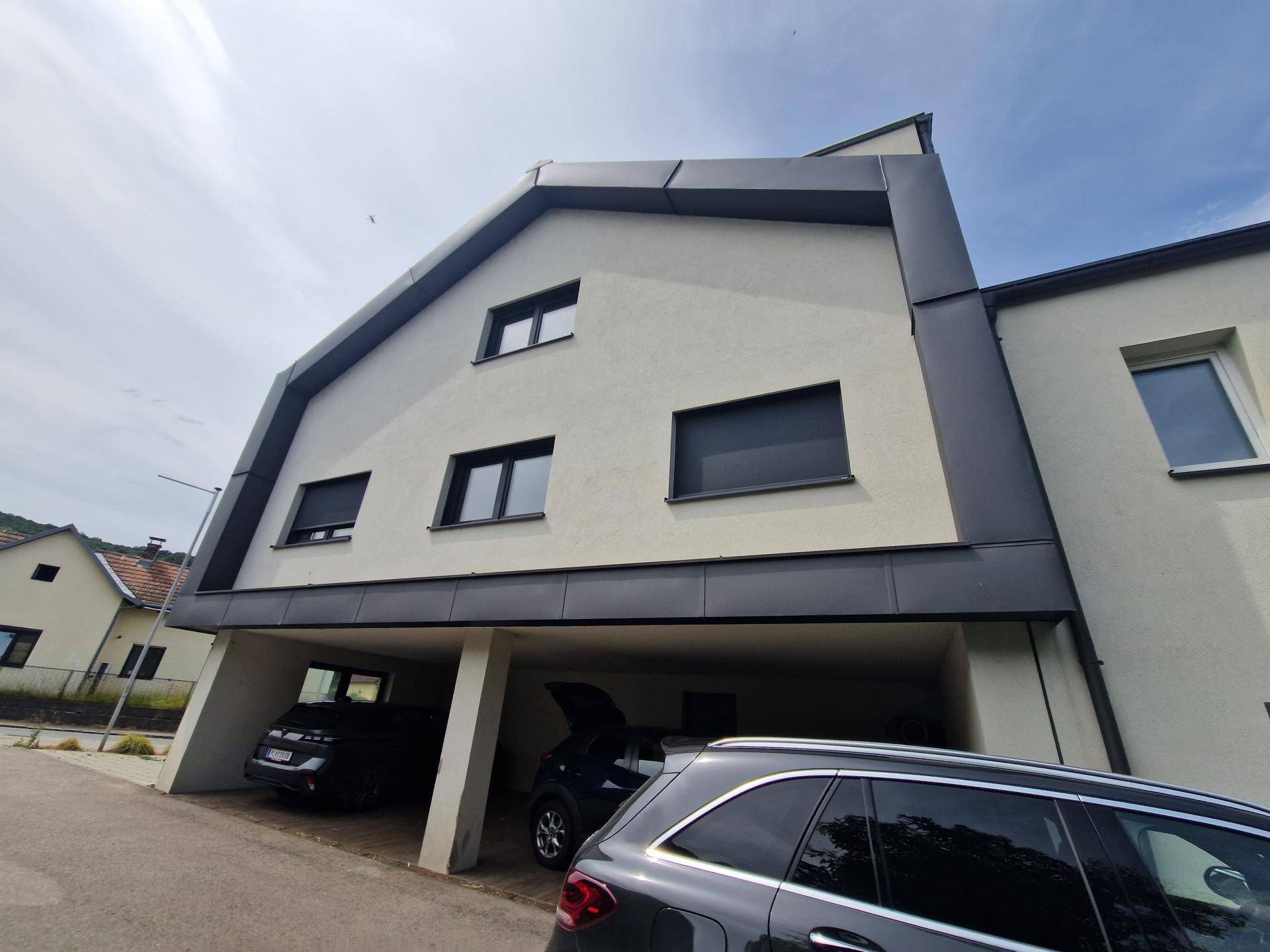 Rückansicht des modernen Gebäudes mit integriertem Carport und weiteren Parkmöglichkeiten im Freien.