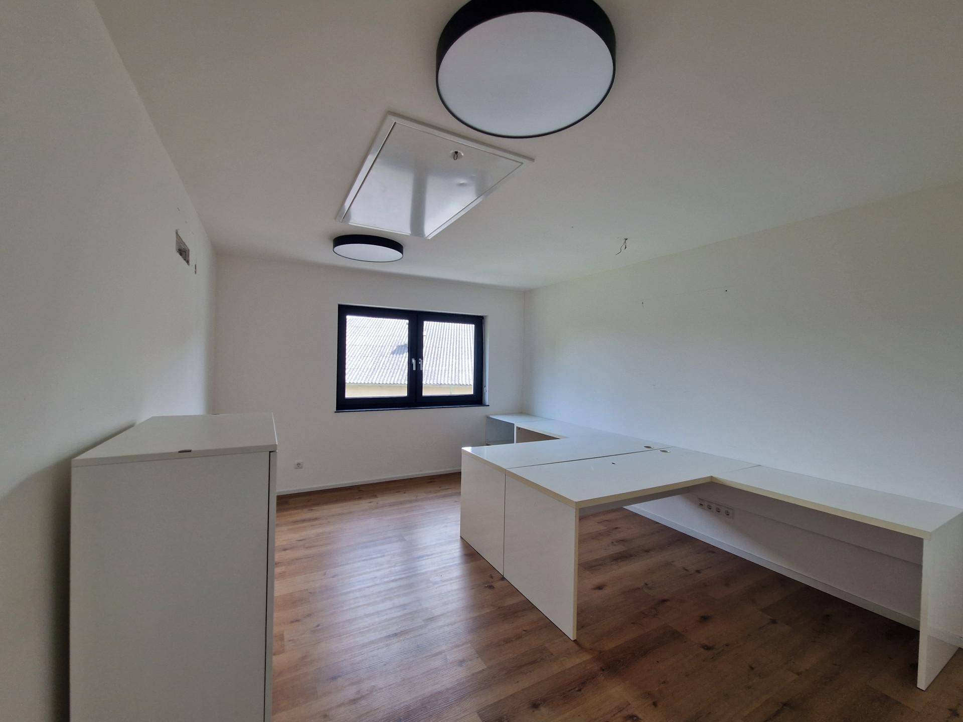 Helles Büro mit modernem Schreibtisch, Holzfußboden und einem Fenster mit Blick ins Grüne.