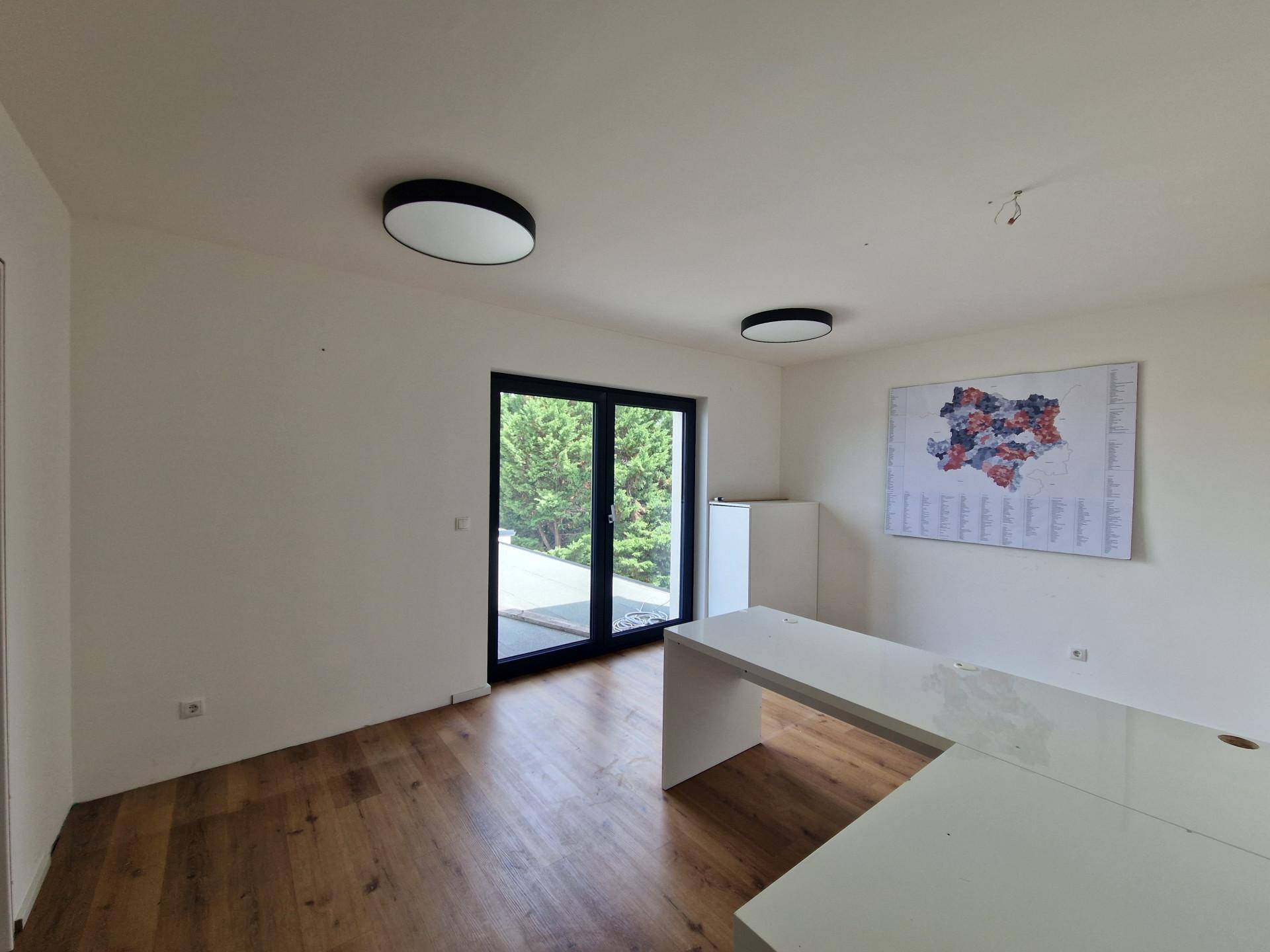 Geräumiges Büro mit Holzboden, modernem Schreibtisch und einer großen Glastür mit Zugang nach draußen.