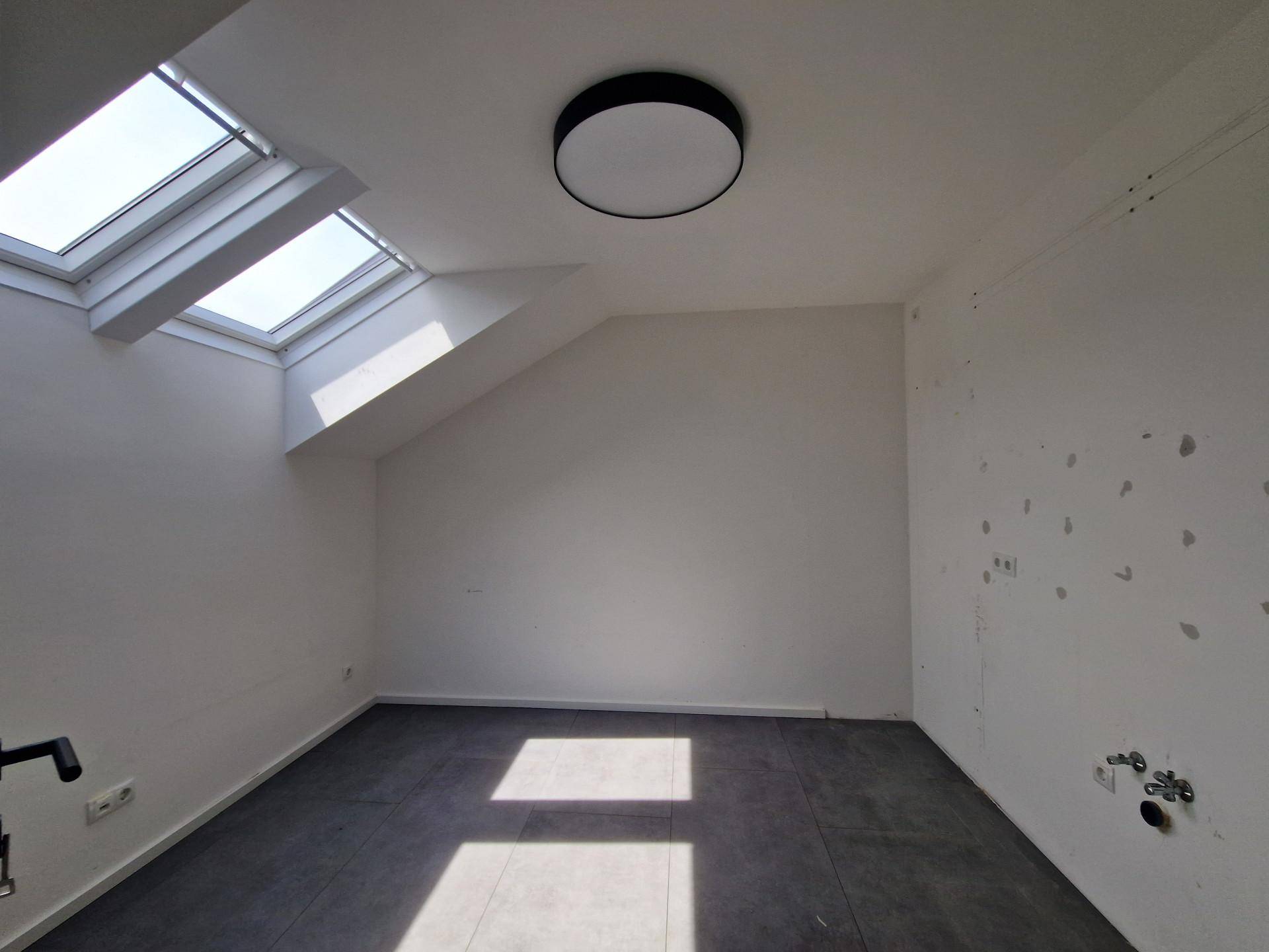 Heller Raum im Dachgeschoss mit dunklem Fliesenboden und mehreren Dachfenstern für viel Tageslicht.