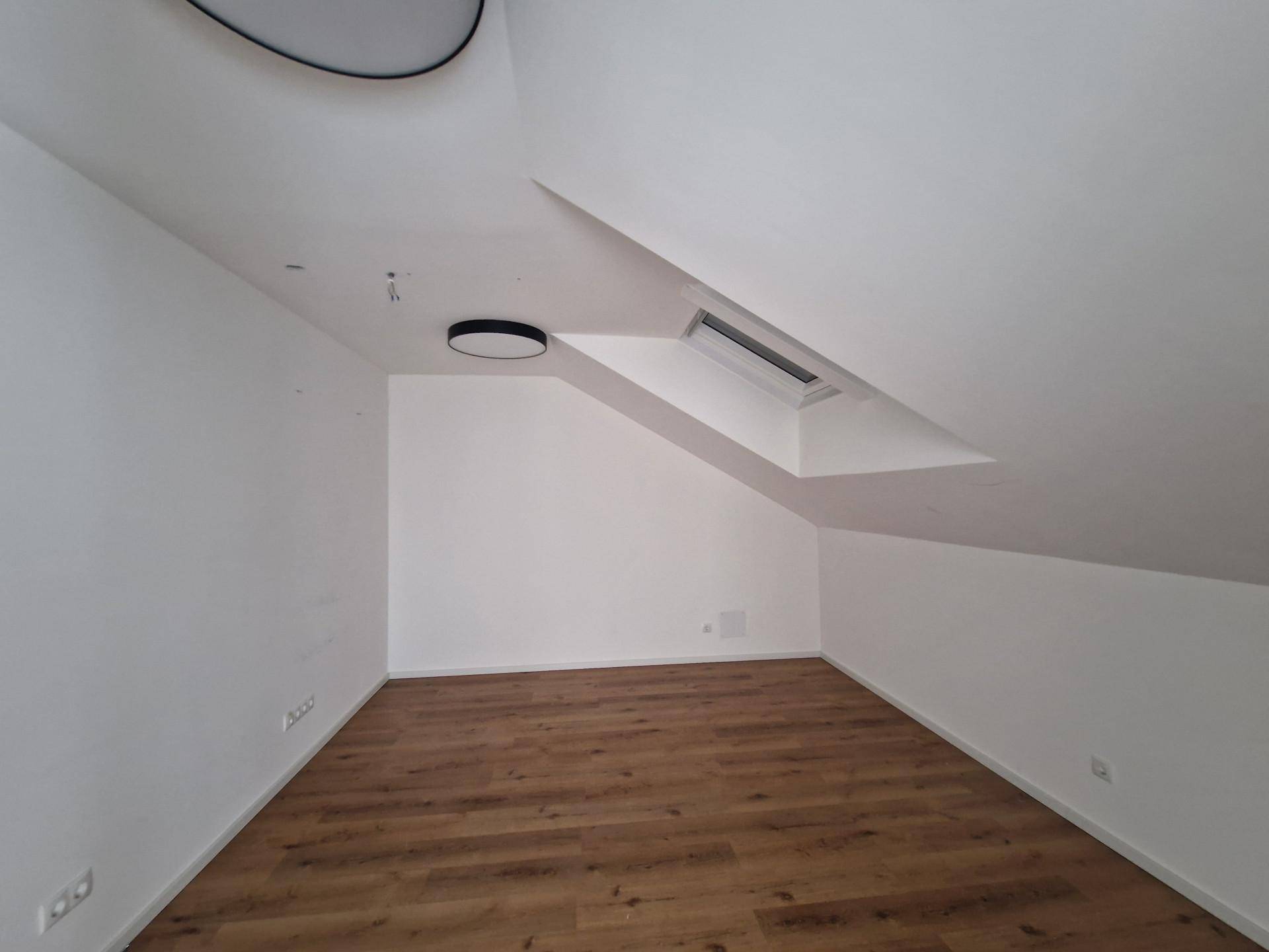 Dachgeschossraum mit hellem Holzboden, schrägen Wänden und einem Dachfenster für natürliche Belichtung.