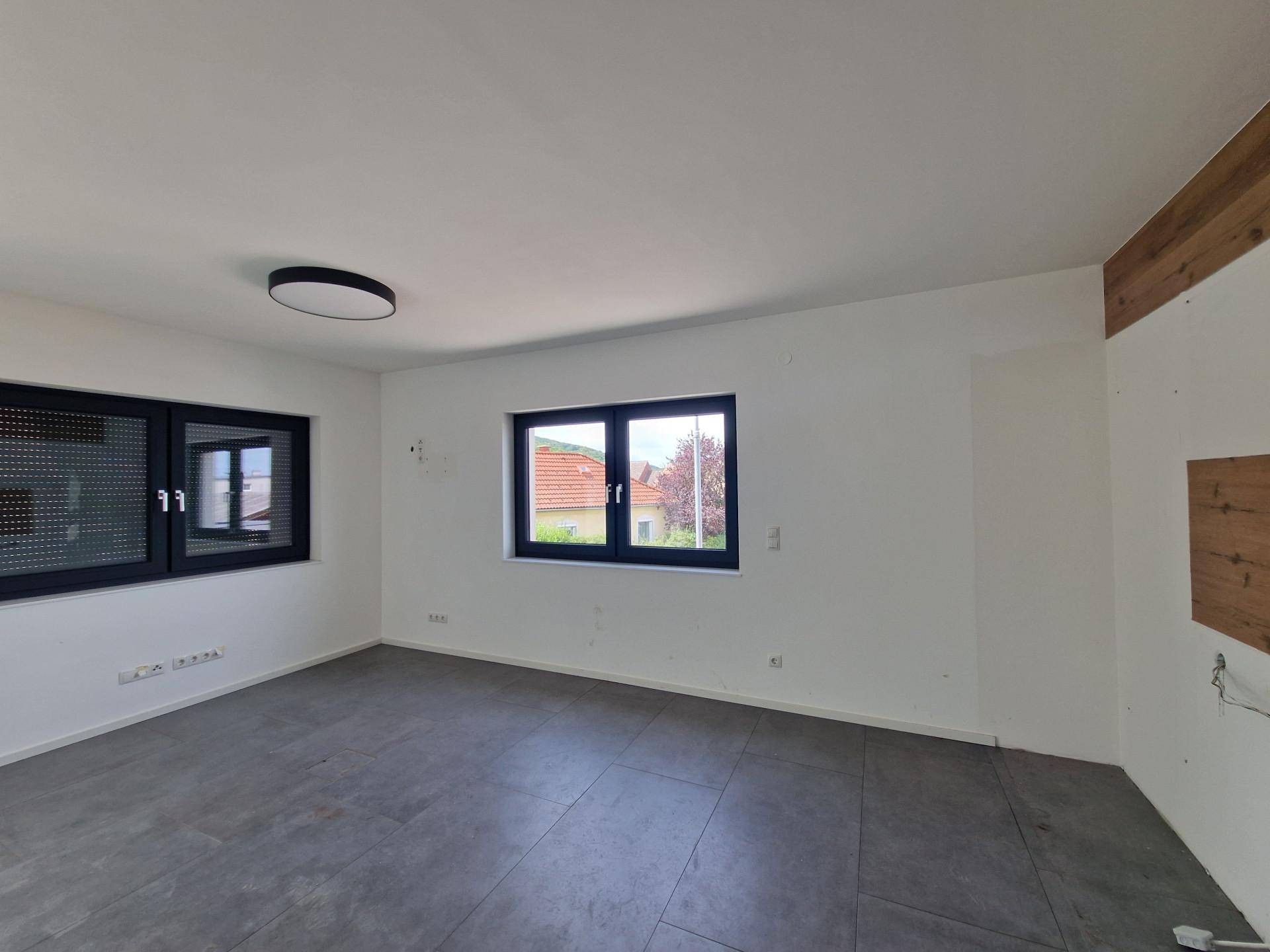 Heller Raum mit dunklem Fliesenboden und zwei Fenstern, ergänzt durch eine dekorative Holzverkleidung.