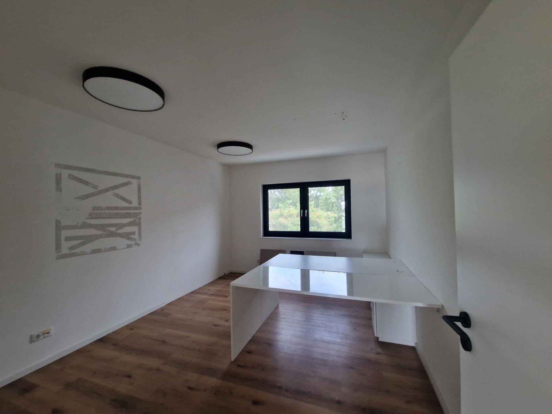 Modernes Büro mit hellem Holzboden, einem Schreibtisch und einem Fenster für natürliche Belichtung.