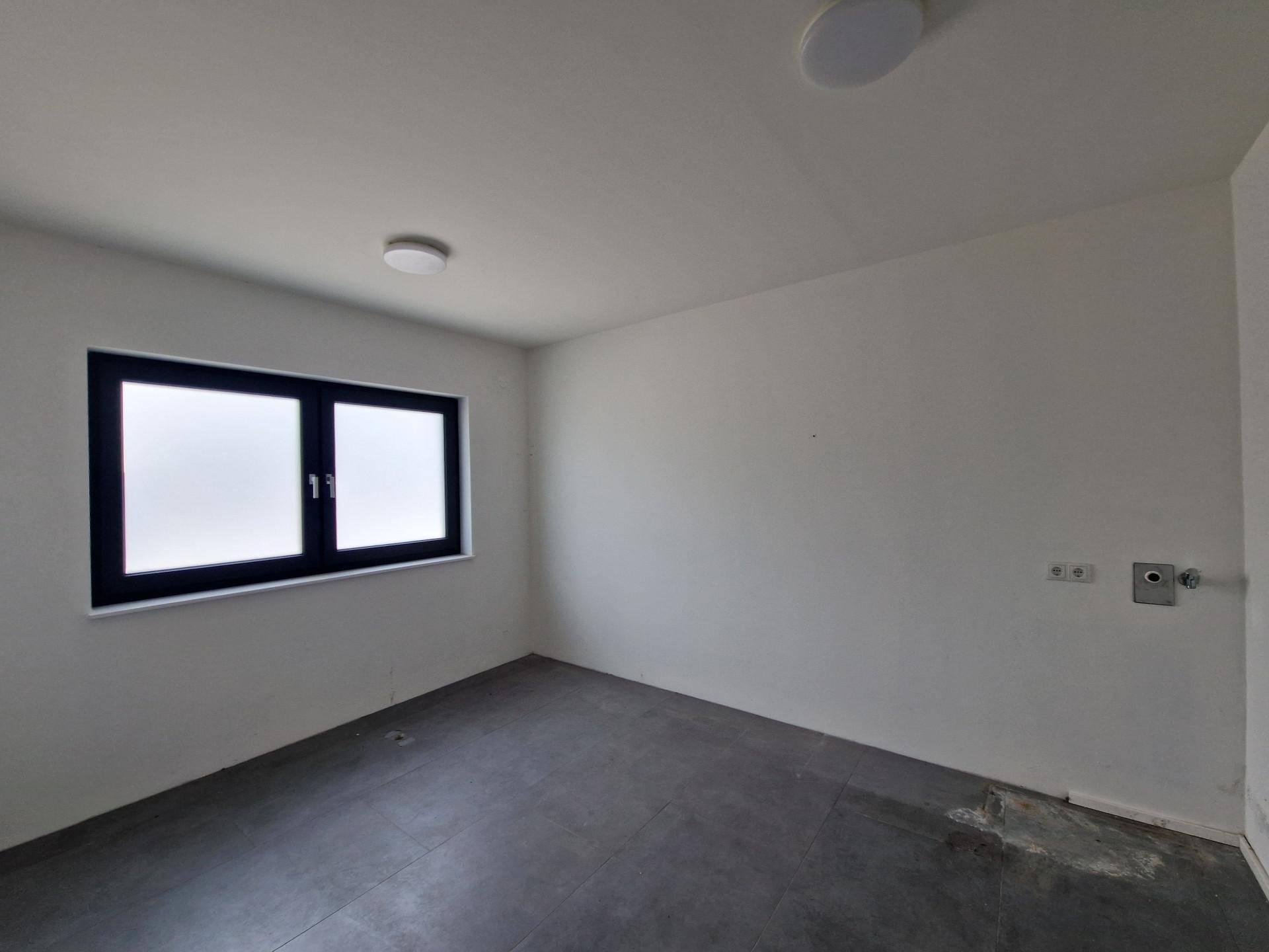 Funktionaler Hauswirtschaftsraum mit dunklem Fliesenboden, Fenster und Anschlüssen für Waschmaschine.