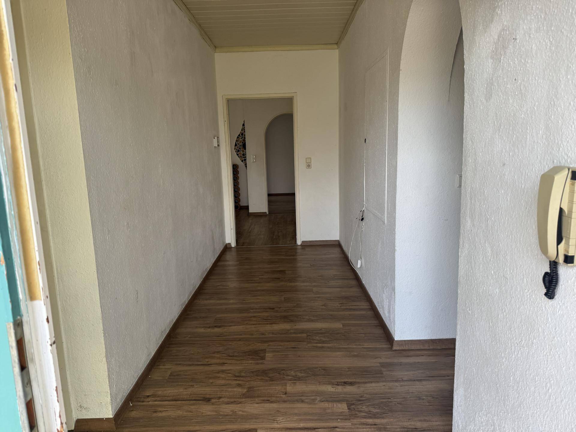 Heller Flur mit Laminatboden und weißen Wänden, der zu weiteren Räumen führt.