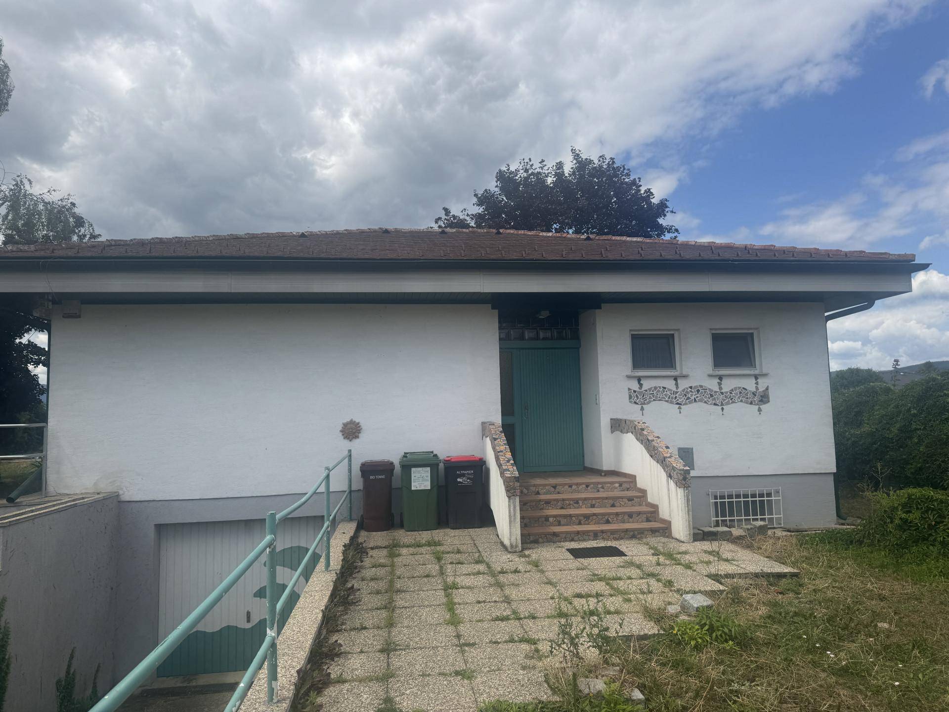 Vorderansicht des Hauses mit Eingangstreppe und Zugang zur Tiefgarage unter bewölktem Himmel.