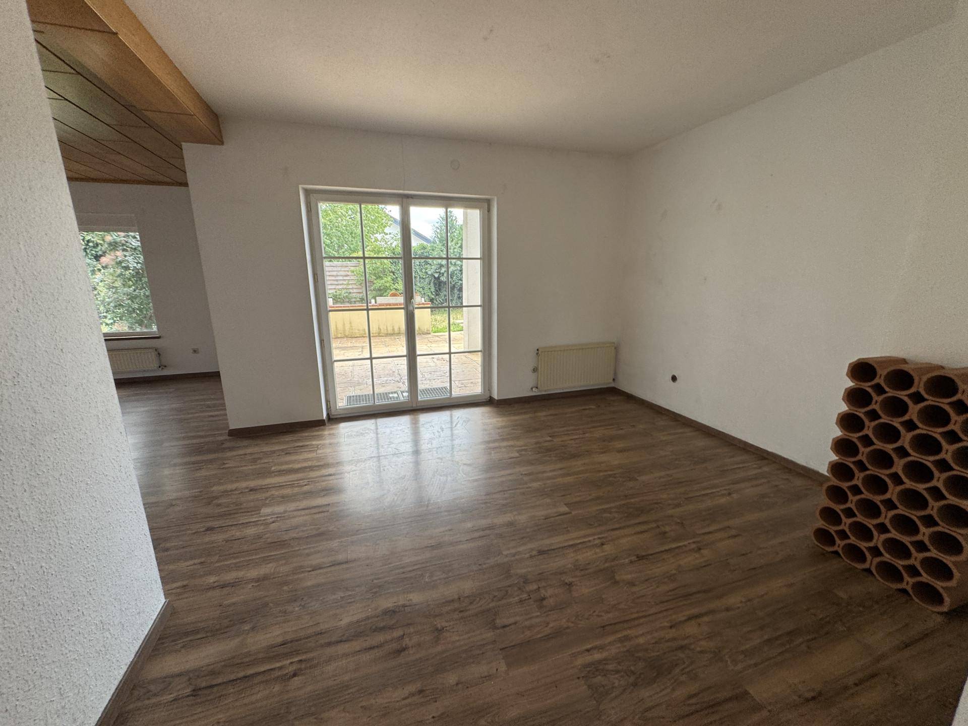 Geräumiges Wohnzimmer mit Laminatboden und großer Glastür, die Zugang zum Außenbereich bietet.