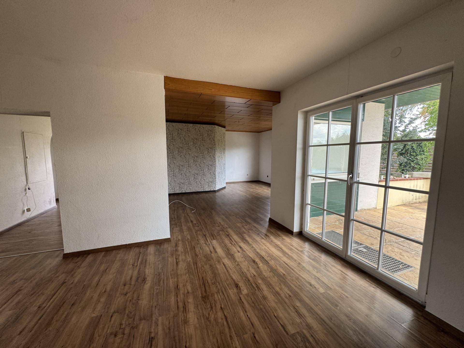 Helles Wohnzimmer mit Holzbalkendecke und großer Glastür, die viel Tageslicht hereinlässt.