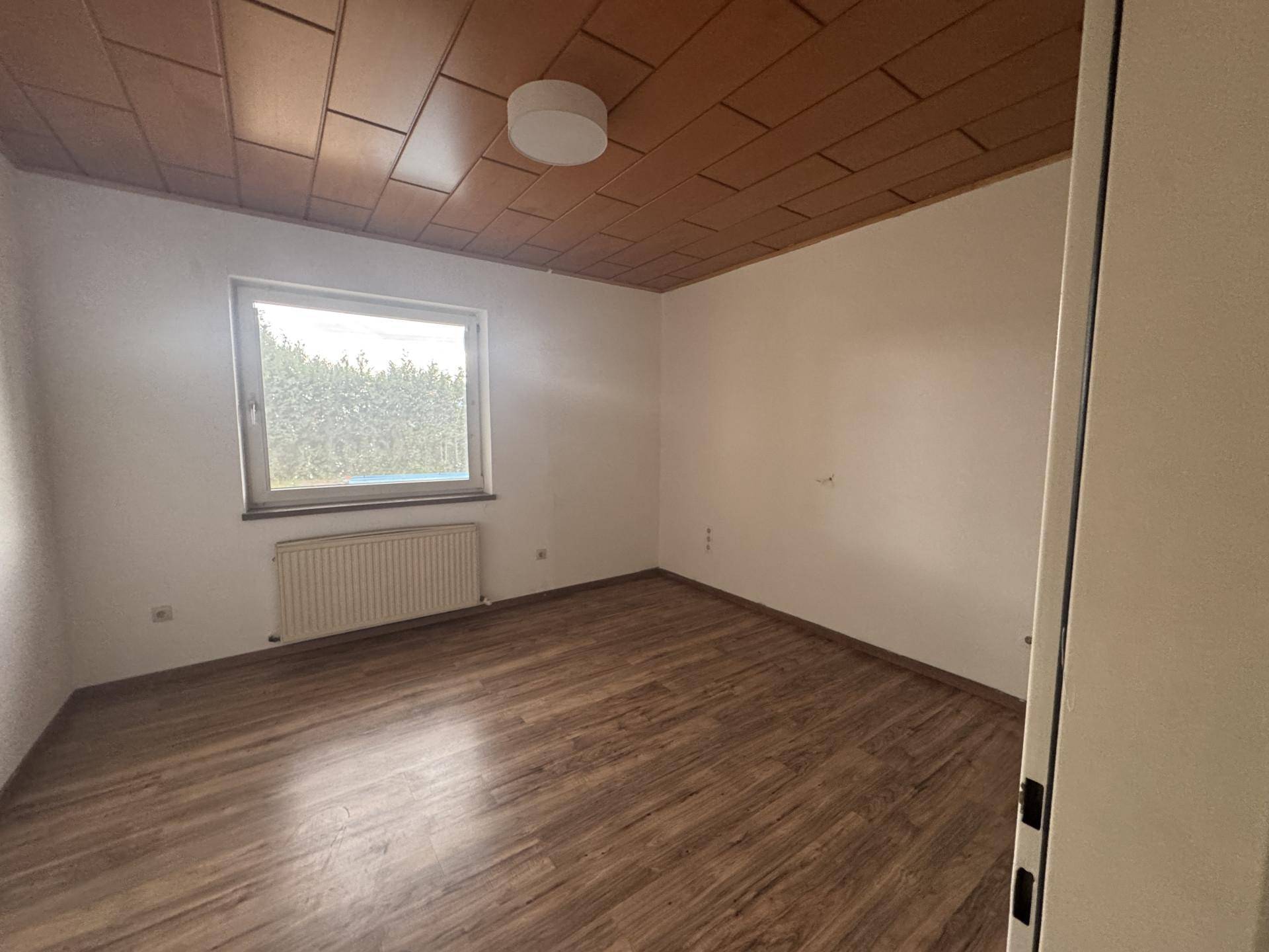 Schlafzimmer mit Laminatboden, weißen Wänden und einem Fenster, das viel Tageslicht bietet.