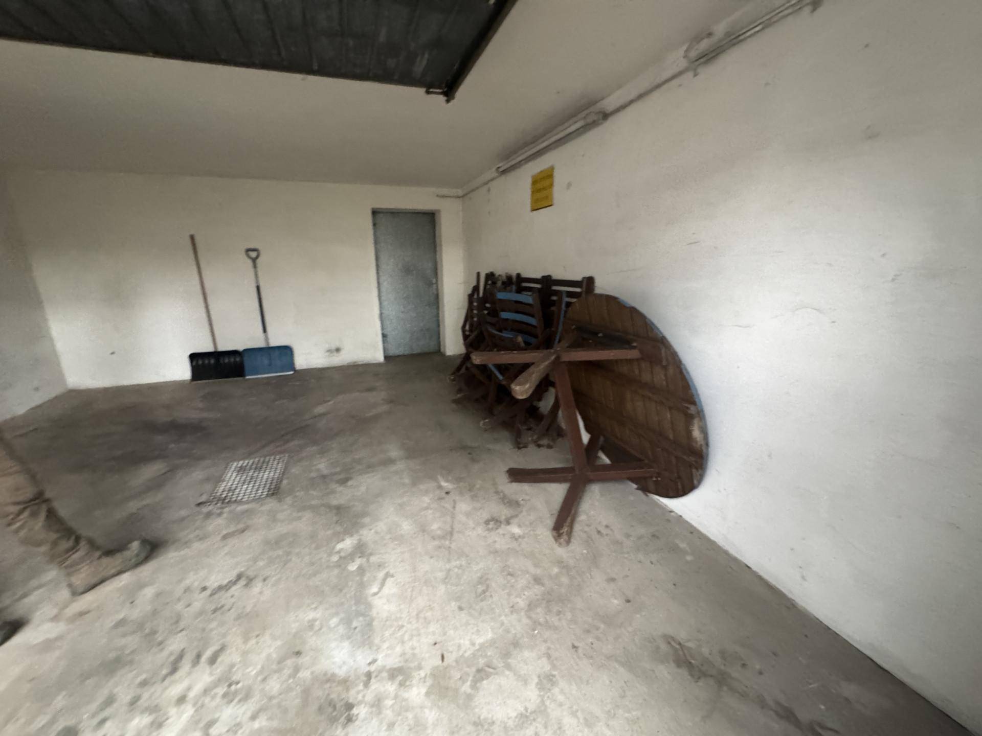 Geräumige Garage oder Abstellraum mit Betonboden und Stauraum für verschiedene Gegenstände.
