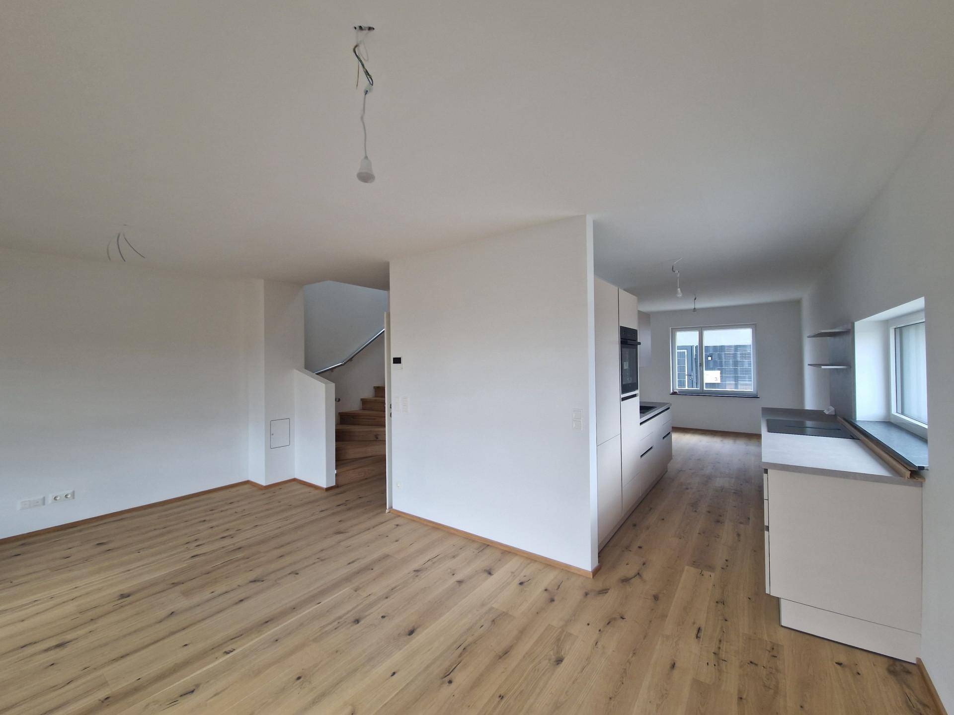 Heller offener Wohnbereich mit neuem Holzboden und Blick auf die moderne Küche und Treppe.