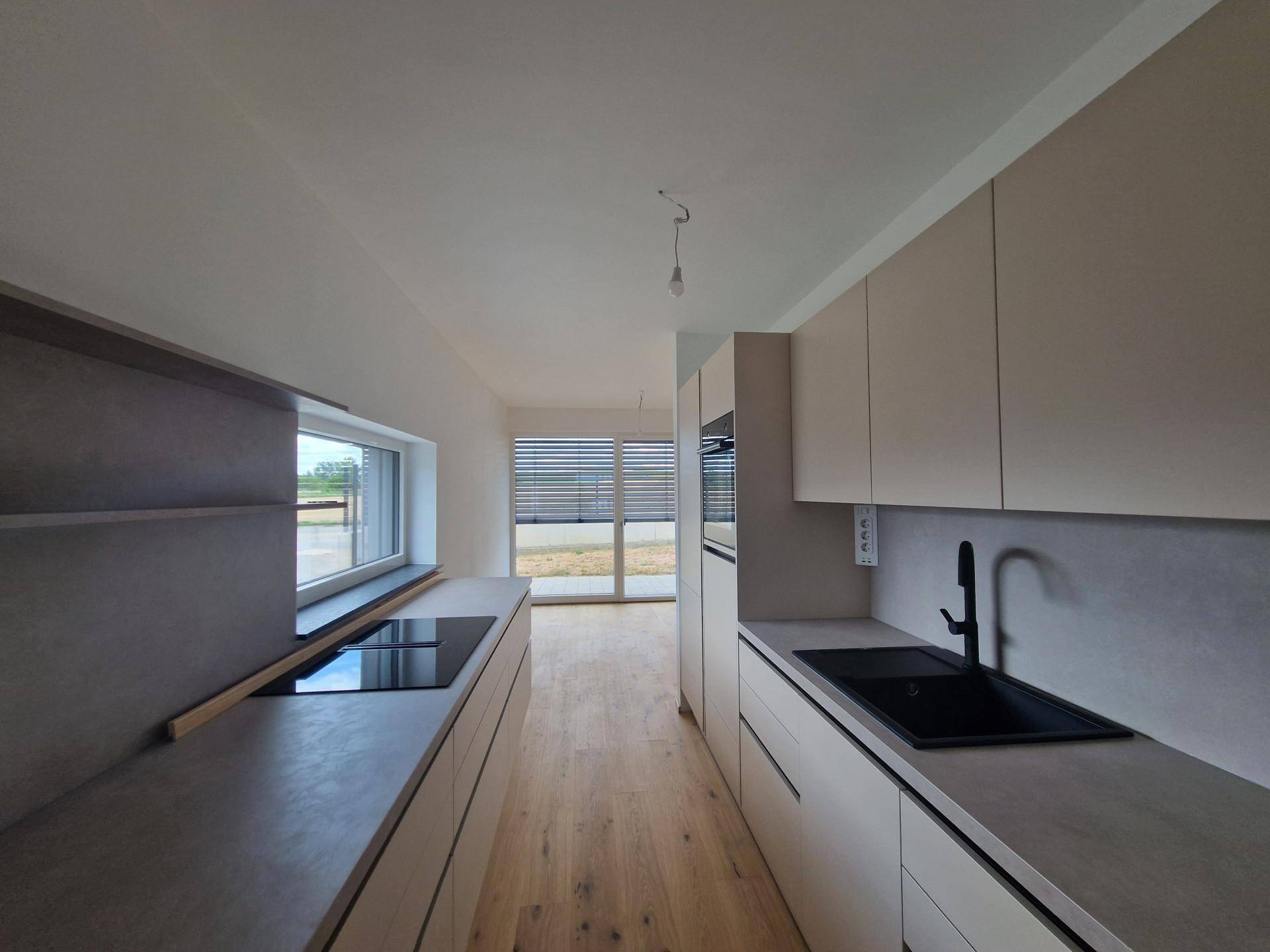 Moderne Einbauküche mit Induktionskochfeld, Spüle und Blick ins Grüne durch das Fenster.