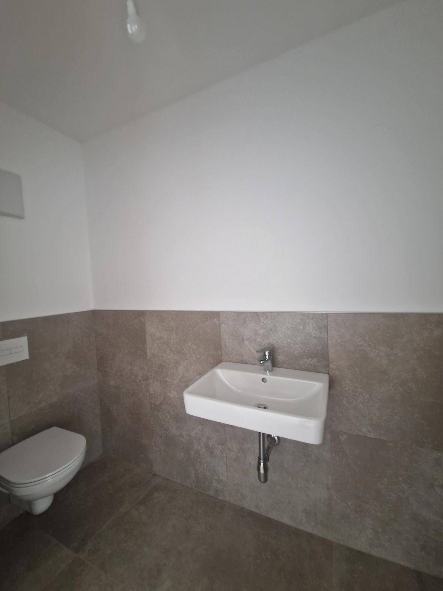 Modernes Gäste-WC mit Wand-WC, kleinem Waschbecken und grauen Fliesen.