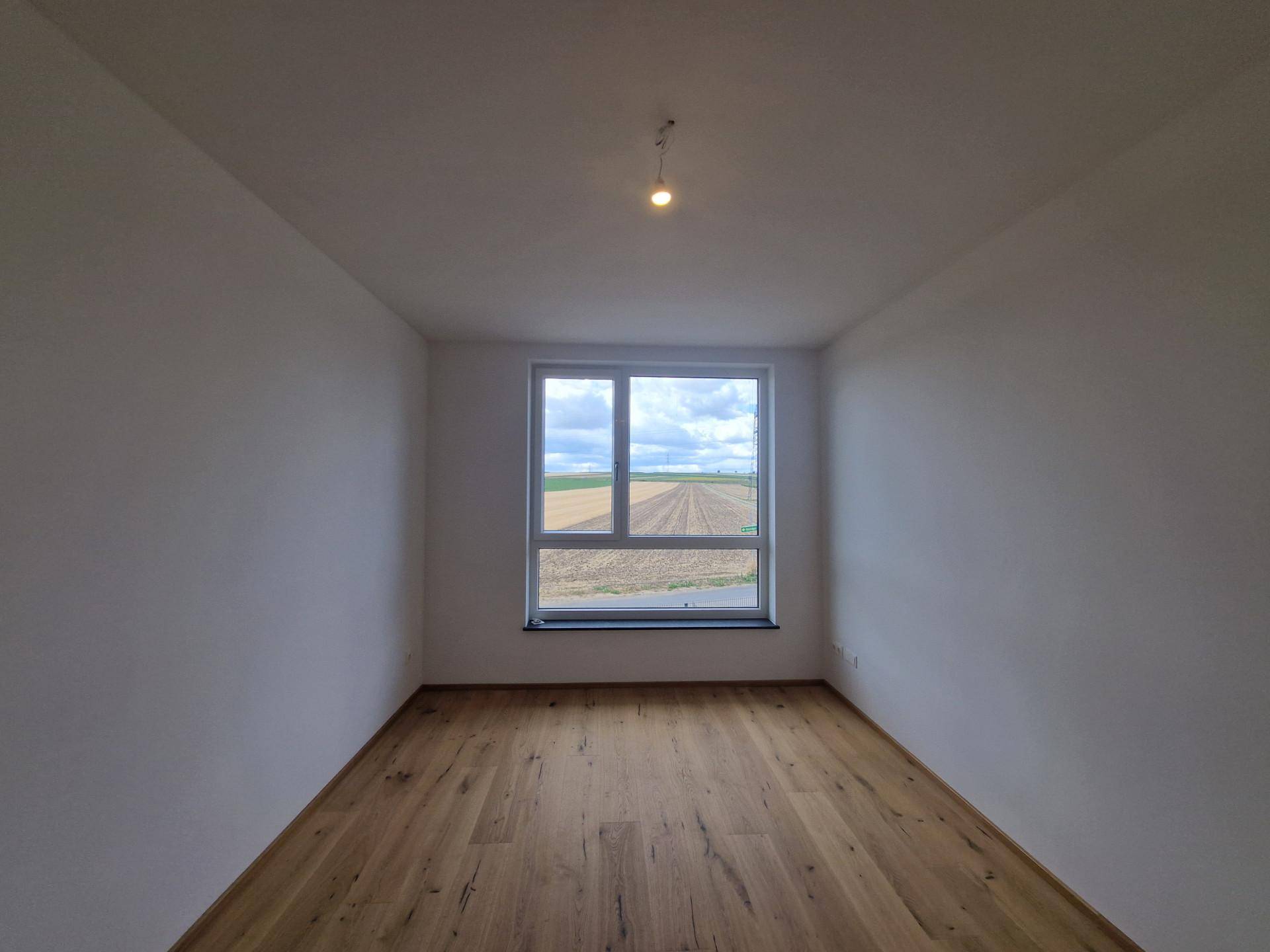 Geräumiges Zimmer mit Holzboden und großem Fenster mit weitem Blick über die Felder.