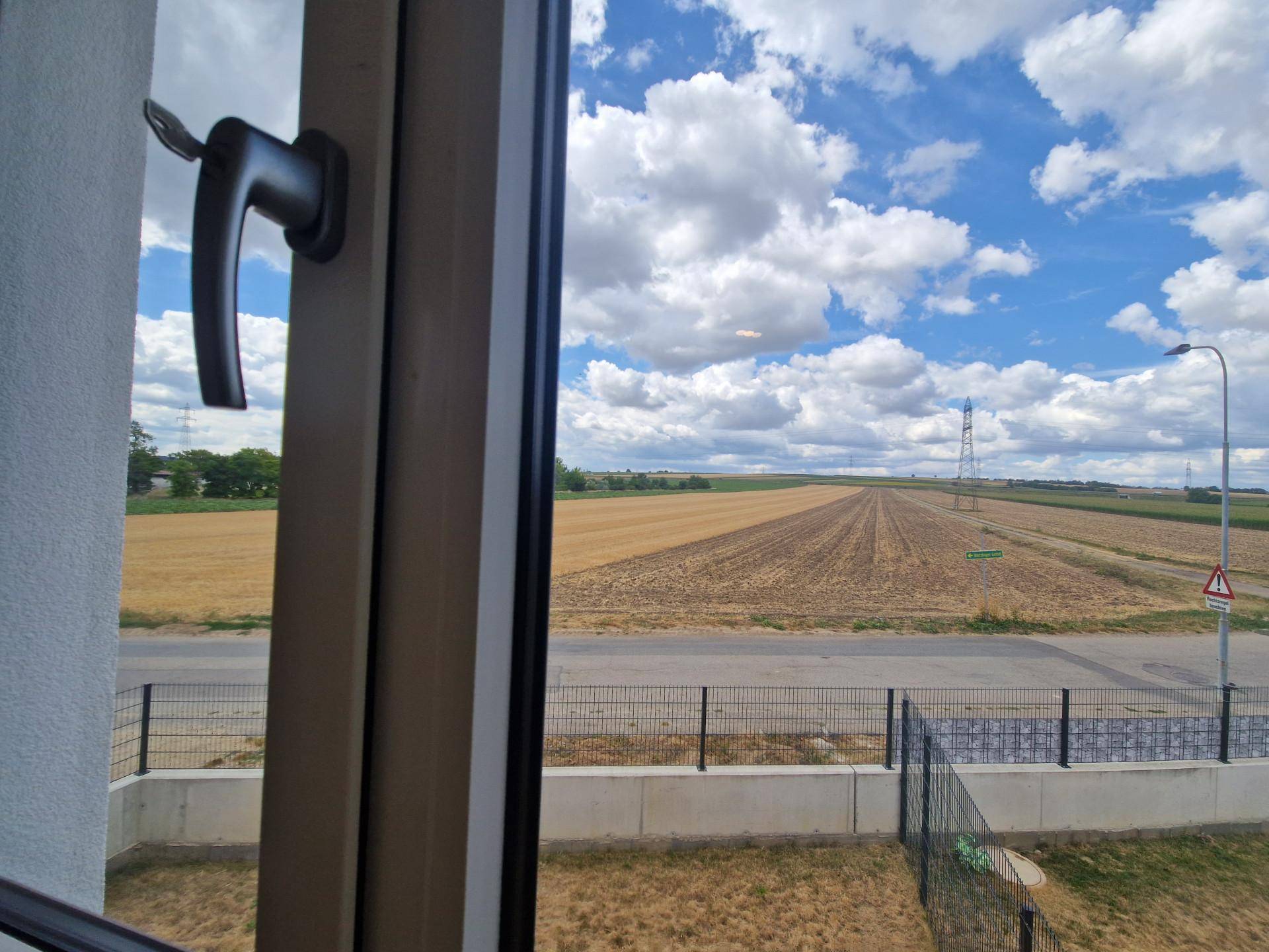 Weitläufiger Blick aus dem Fenster auf die umliegende Landschaft und Felder unter blauem Himmel.