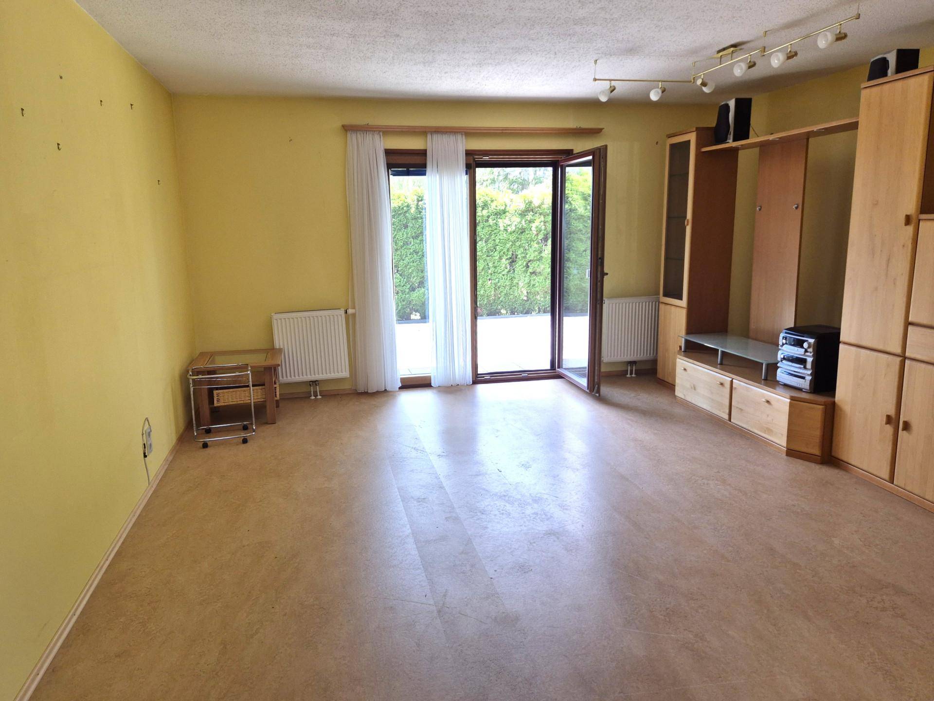 Geräumiges Wohnzimmer mit gelben Wänden, Laminatboden und direktem Zugang zum grünen Gartenbereich.