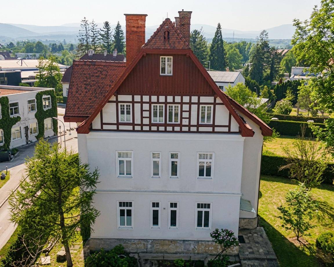 Ansicht der Hausfassade mit traditionellen Elementen, roten Ziegeln und Fachwerkgiebel, umgeben von grüner Landschaft.