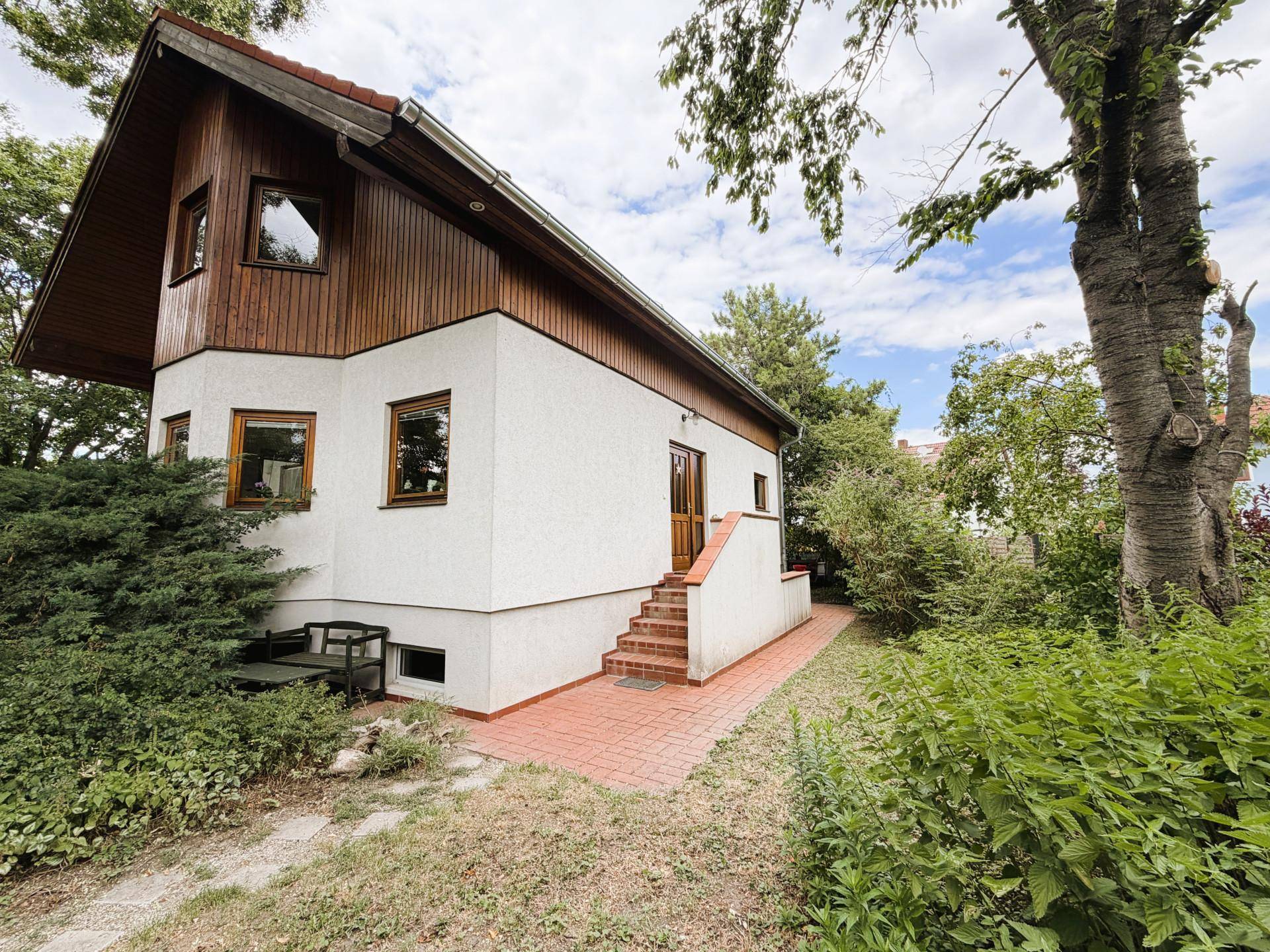 Seitenansicht des Hauses mit weißer Fassade, Holzelementen und Außentreppe zum Eingang.