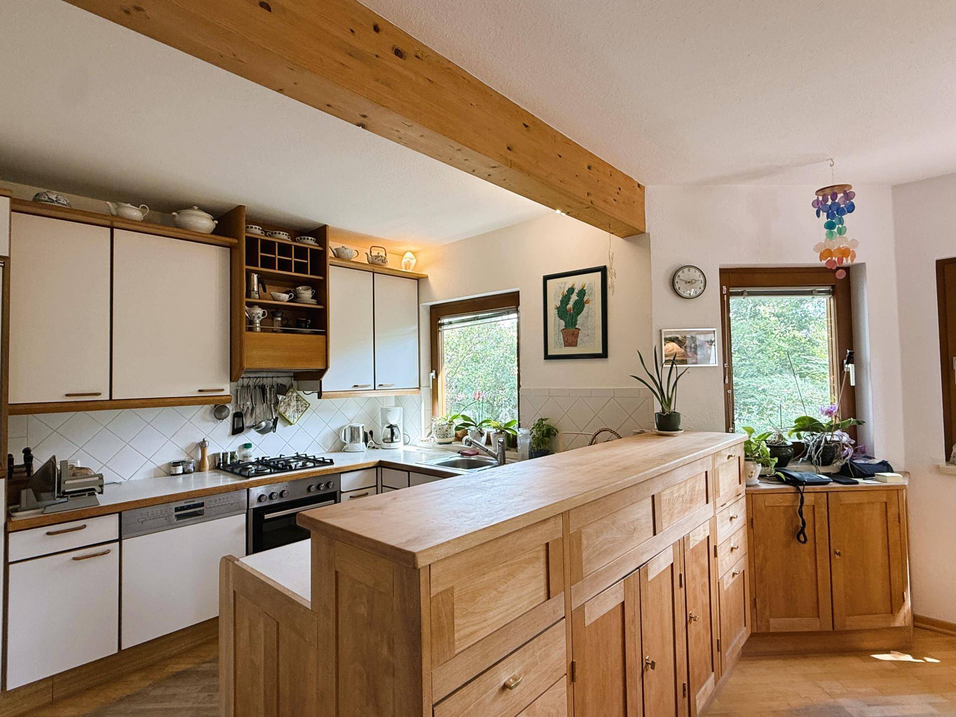 Helle Küche mit weißen Schränken, Holzelementen und Blick in den Garten.