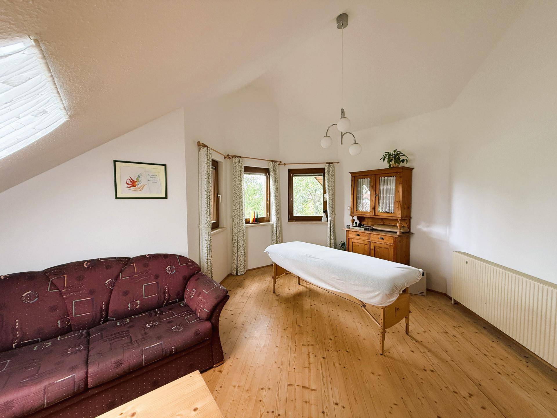 Geräumiges Zimmer im Dachgeschoss mit Sofa, Holzschrank und Fenstern mit Blick ins Grüne.