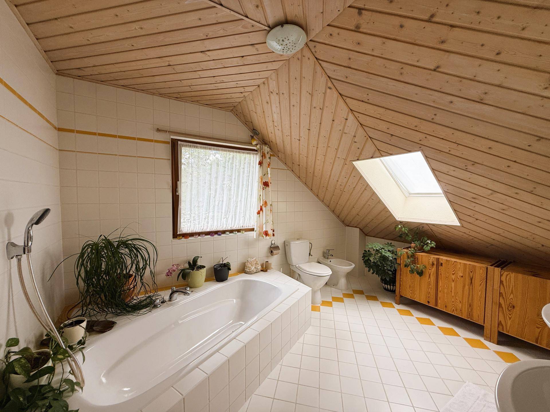 Badezimmer im Dachgeschoss mit Badewanne, Bidet, Holzdecke und Dachfenster.