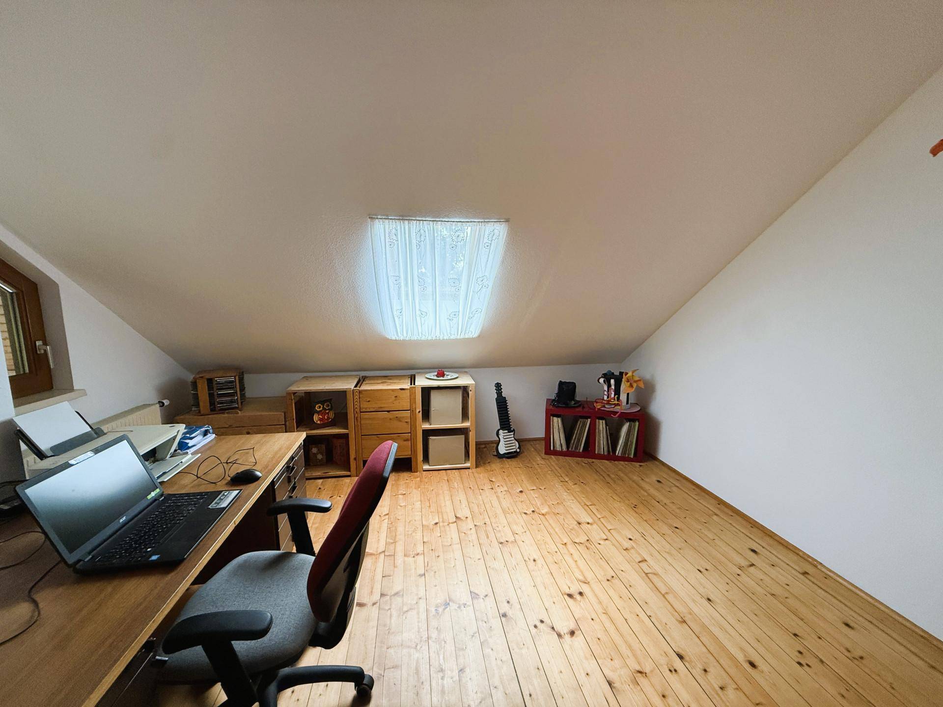 Arbeitszimmer im Dachgeschoss mit Holzboden, Schreibtisch und Dachfenster für natürliches Licht.