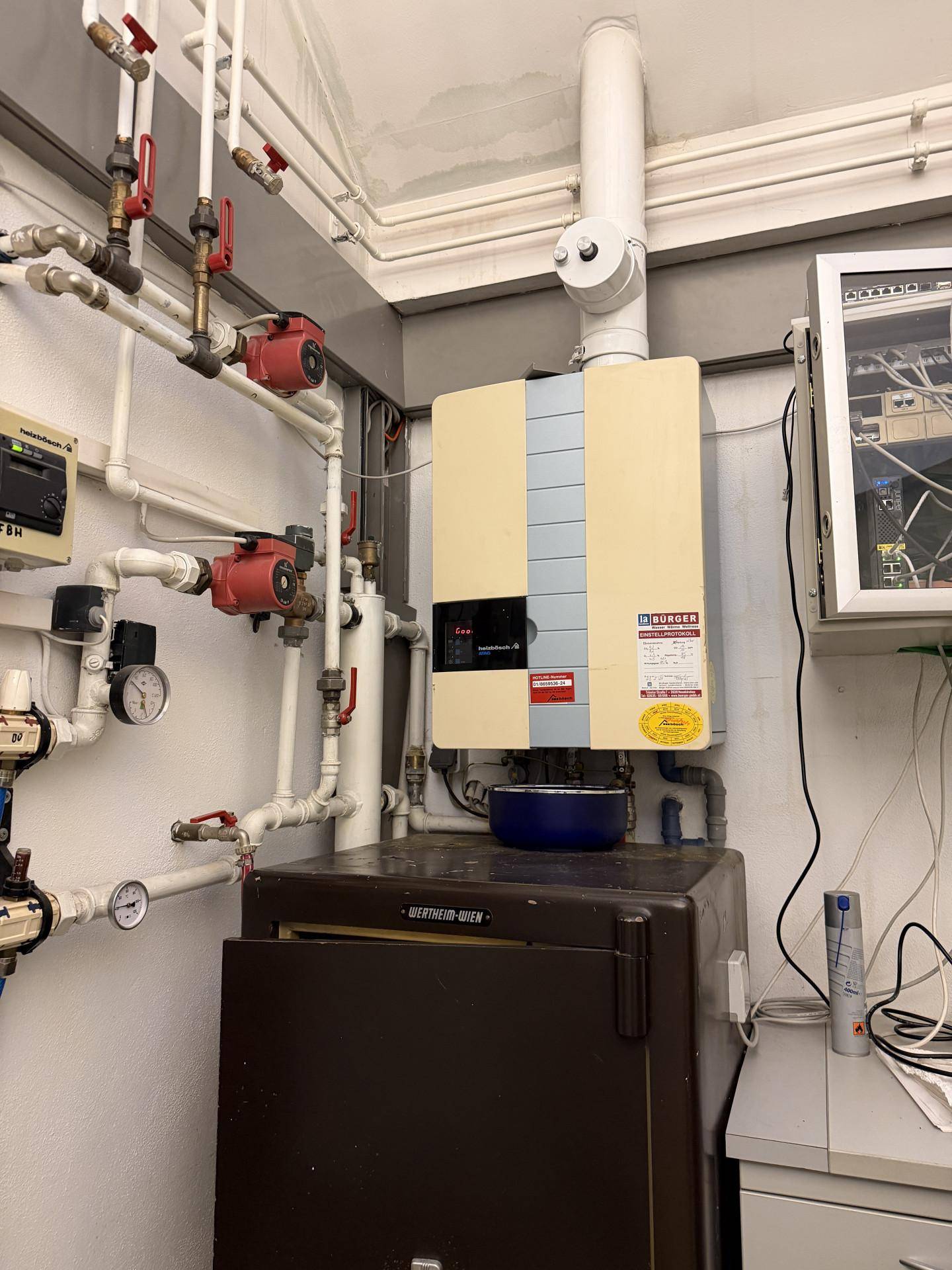 Technikraum mit Heizungsanlage, Rohren und einem Safe an der Wand.