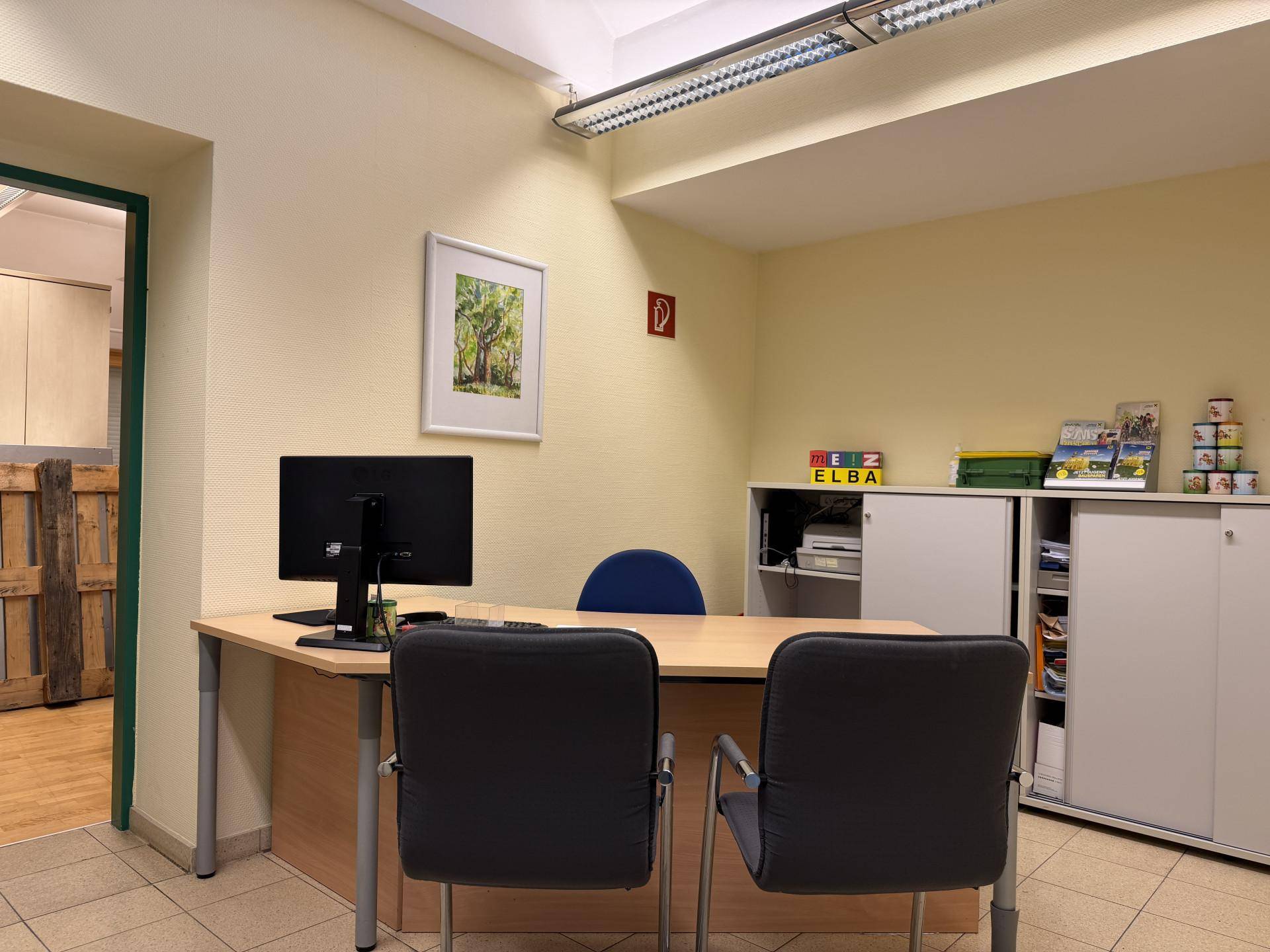Möbliertes Büro mit Schreibtisch, Bürostühlen und Aktenschränken in hellem Ambiente.