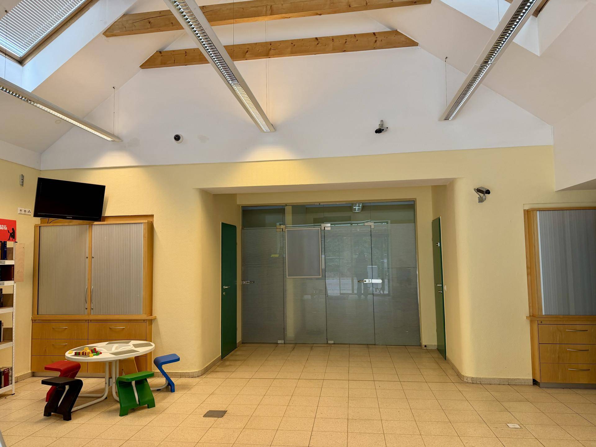 Großer offener Bereich mit Kinderspielecke, Fliesenboden und hohen Decken mit Dachfenstern.