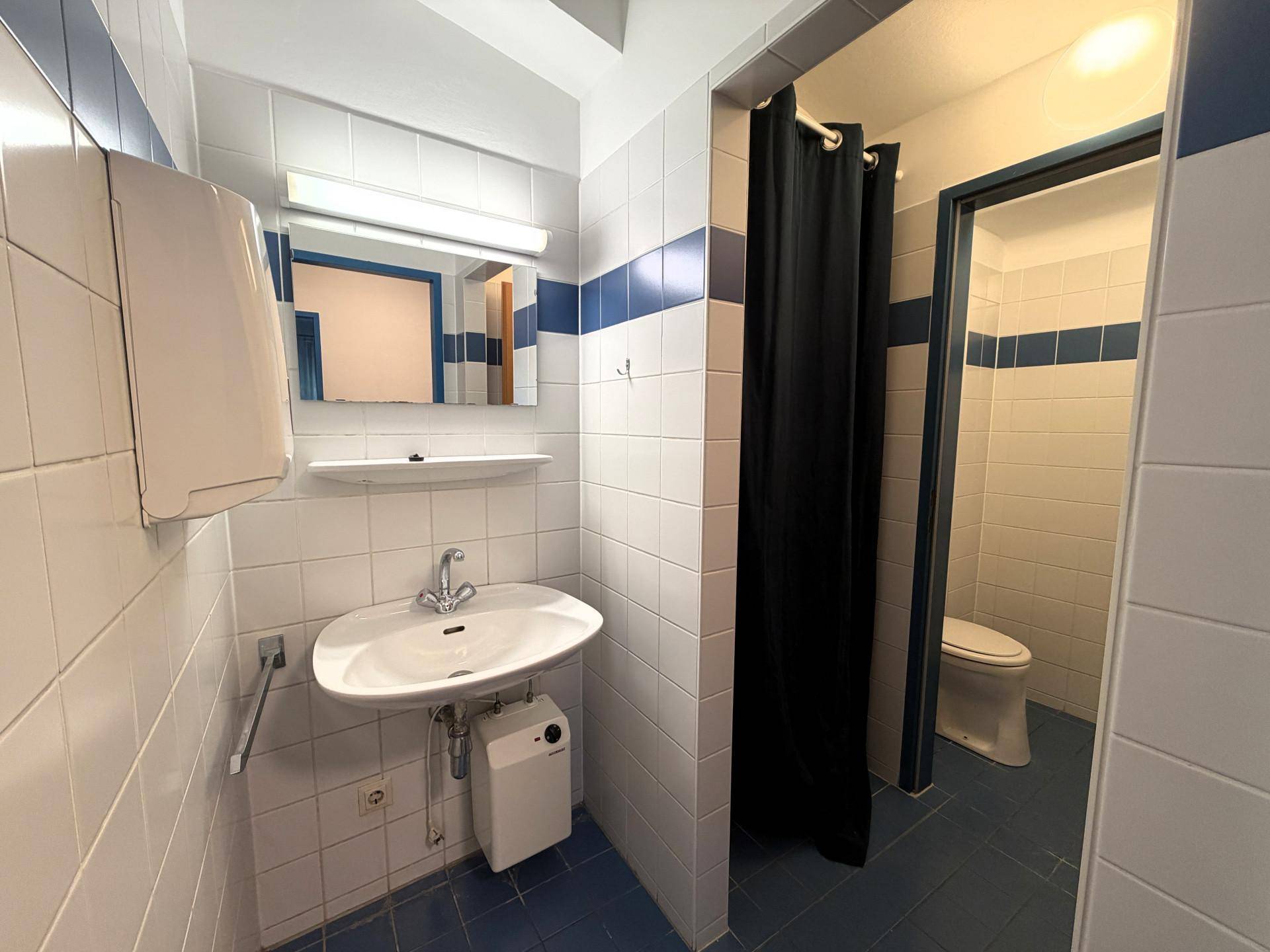 Badezimmer mit weißen und blauen Fliesen, Waschbecken und Duschbereich hinter einem schwarzen Vorhang.